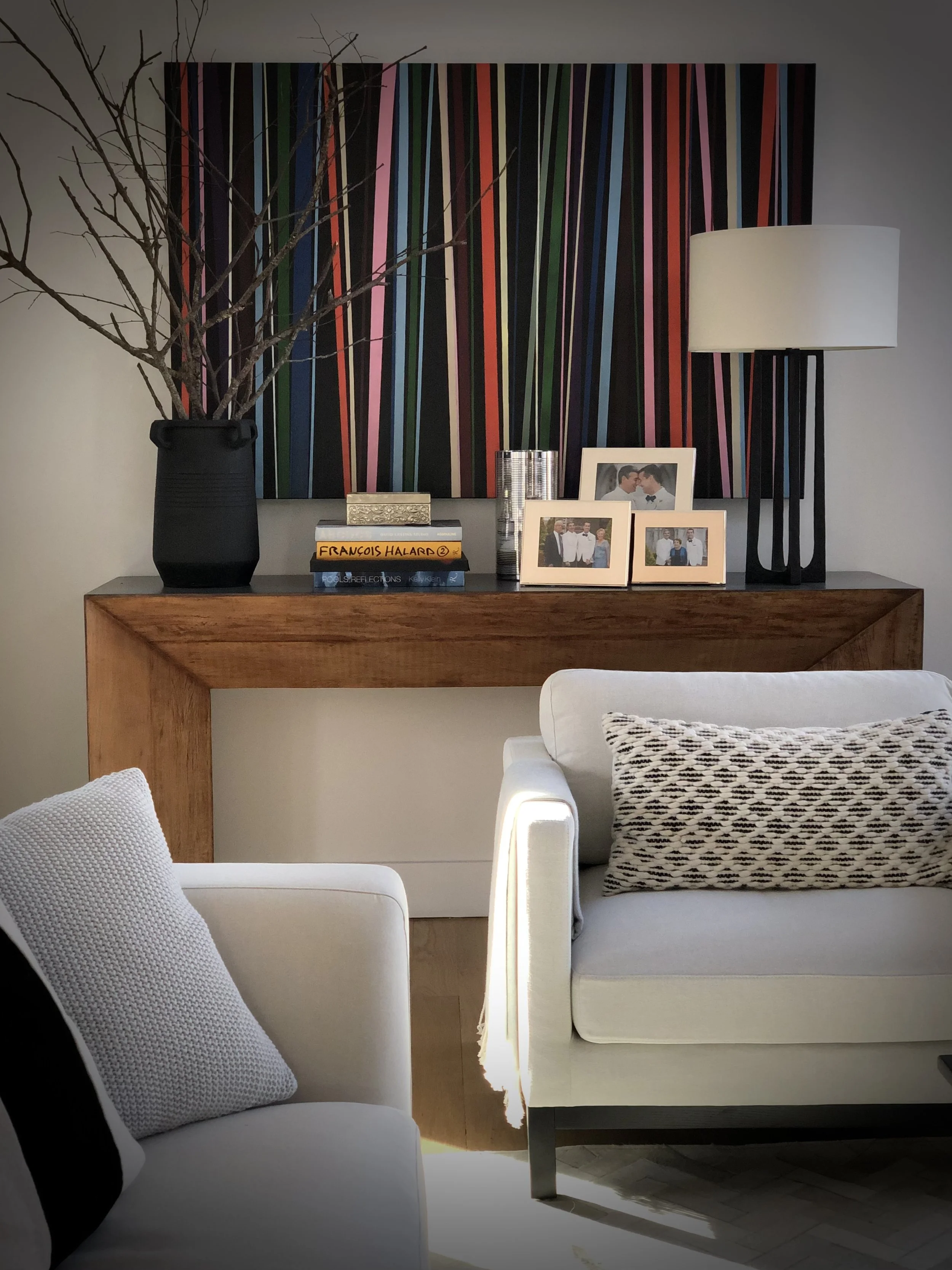 Wood console styled with books, framed photos, and ceramic vessels beneath a bold striped artwork in a calm living space