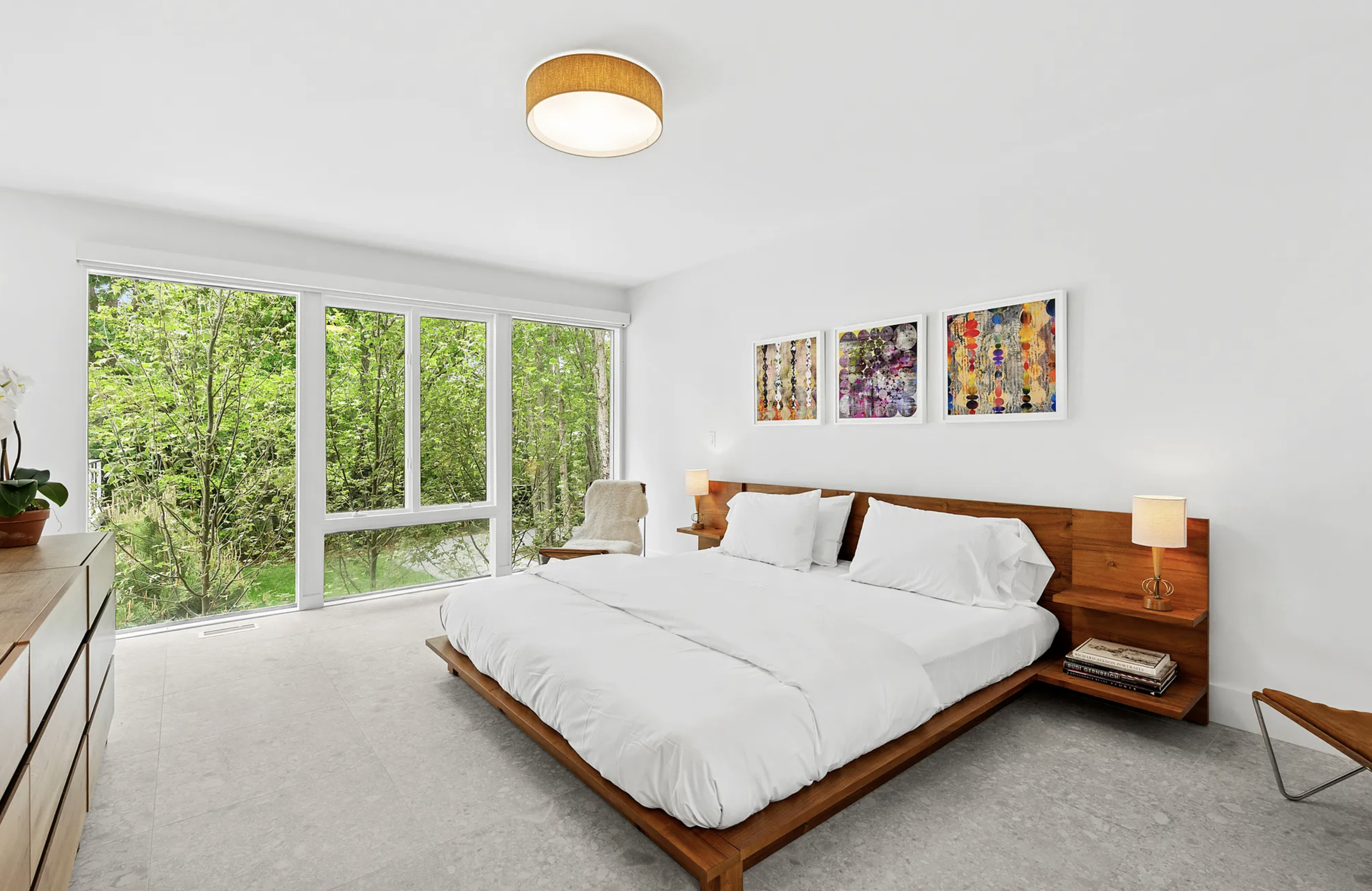 Serene bedroom with a low-profile wood bed, white bedding, large windows, and views of surrounding trees.