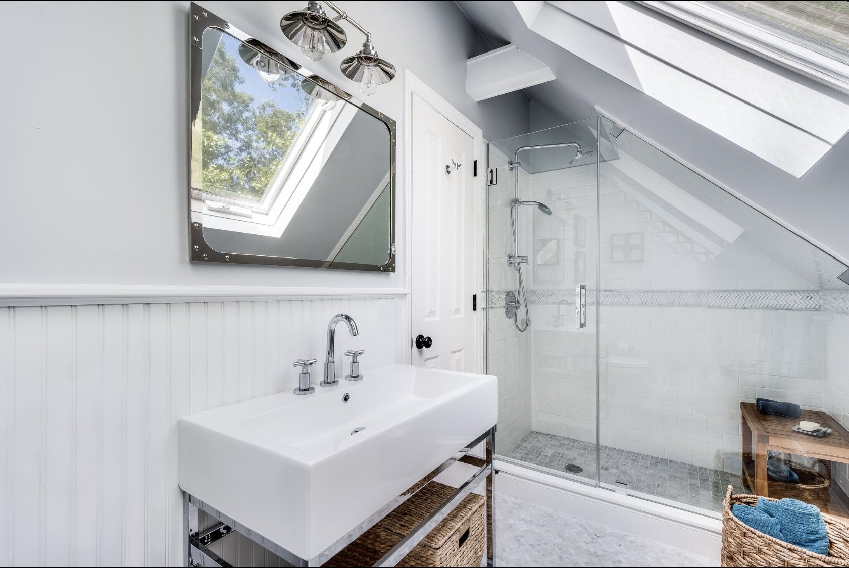 Bright bathroom with skylight, glass-enclosed shower, white beadboard walls, and a compact vanity designed for an attic space