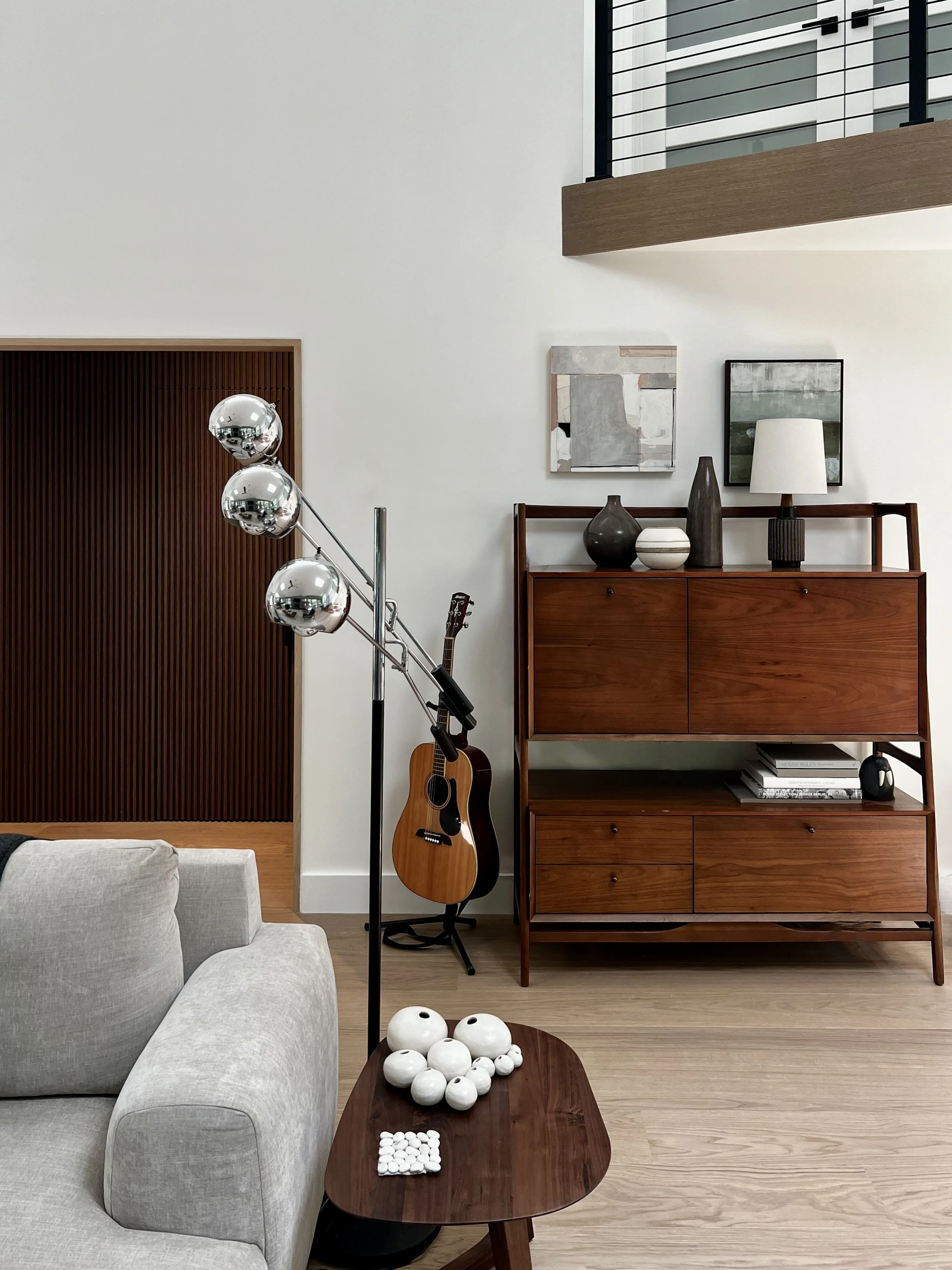 Modern living area with warm wood furnishings, sculptural floor lamp, and a mid-century credenza set against white walls and vertical wood paneling
