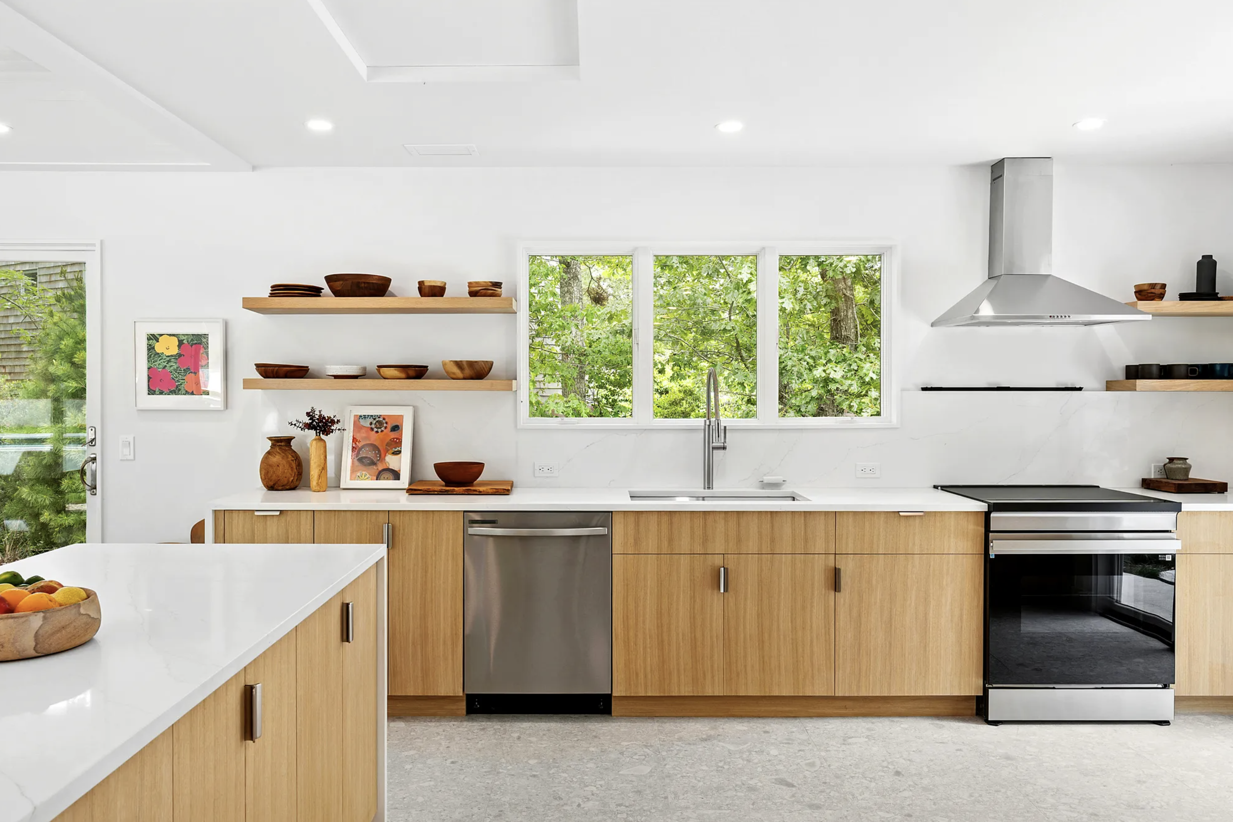 Bright kitchen with white countertops, light wood cabinetry, open shelving, and garden views