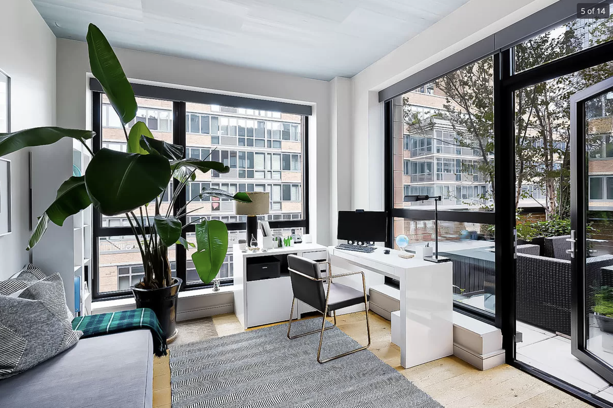 Light-filled urban home office with large windows, built-in desk, and indoor plant