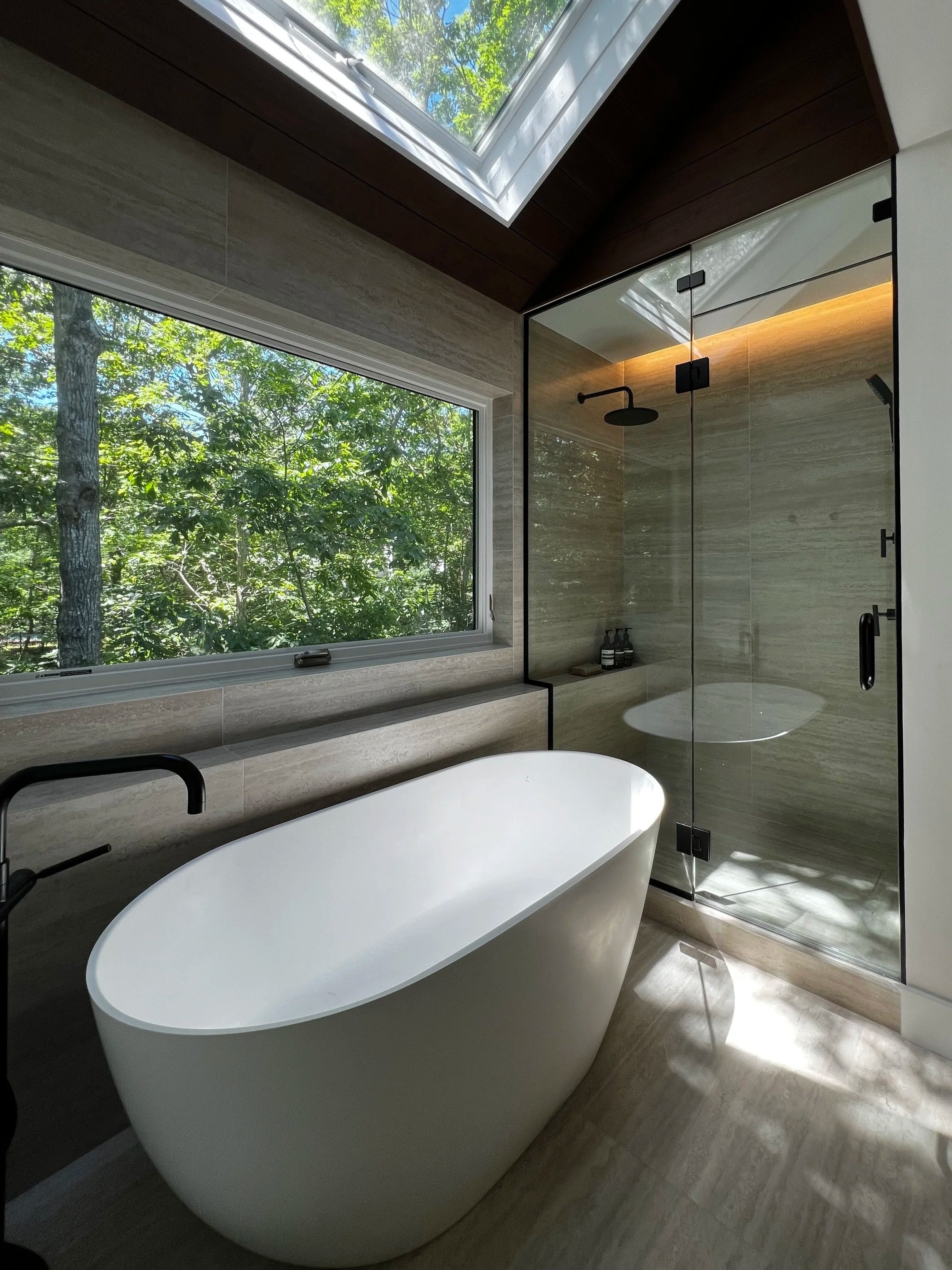 contemporary bathroom with travertine floors, soaking tub, skylight and picture window to the greenery