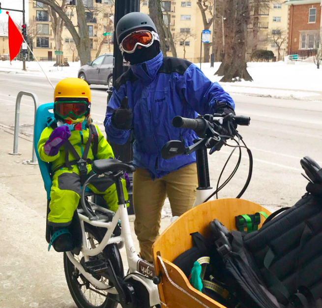 woman with toddler wearing full cold weather gear and goggles on a cargo bike