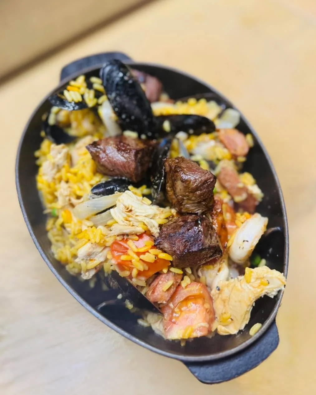 Paella Perfection: saffron-infused yellow rice saut&eacute;ed with chicken, shrimp, mussels, andouille sausage, steak tid-bits, caramelized onions, tomatoes &amp; sweet peas 🥘