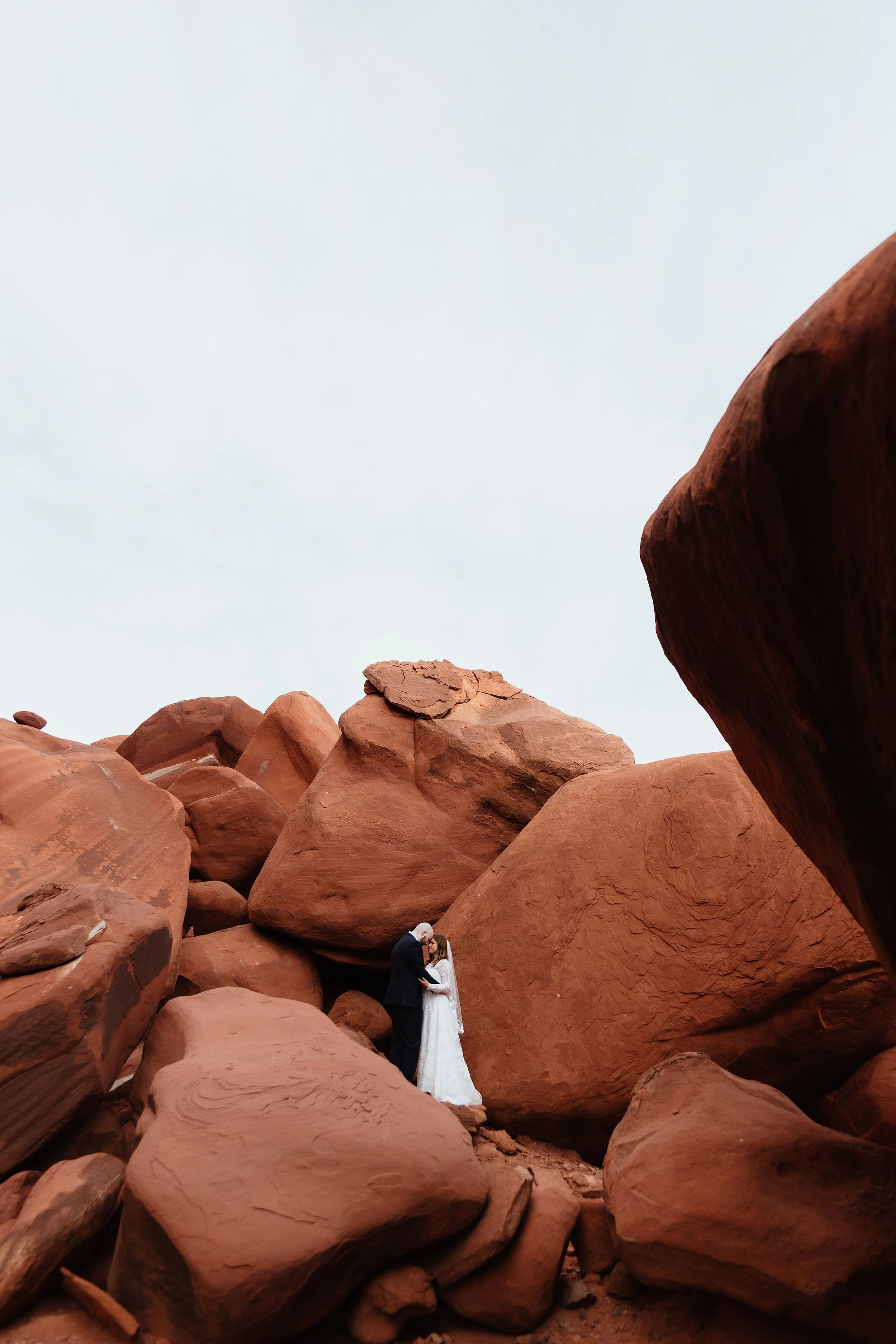 A bride and groom are embracing on in the middle of a red rock boulder field