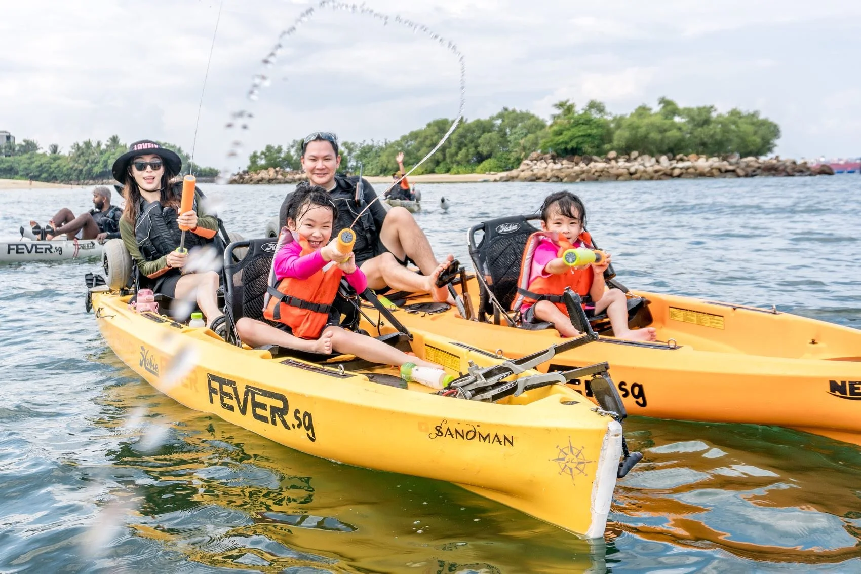 Family of 4 with 2 little girls kayaking in Sentosa, little girl fired a jet of water from her water gun towards the camera.