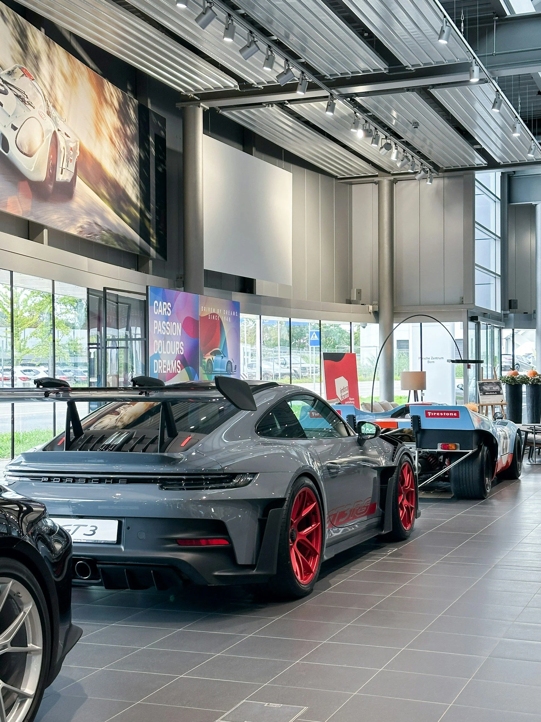 Gray Porsche 911 GT3 with red wheels on display inside a modern car showroom.