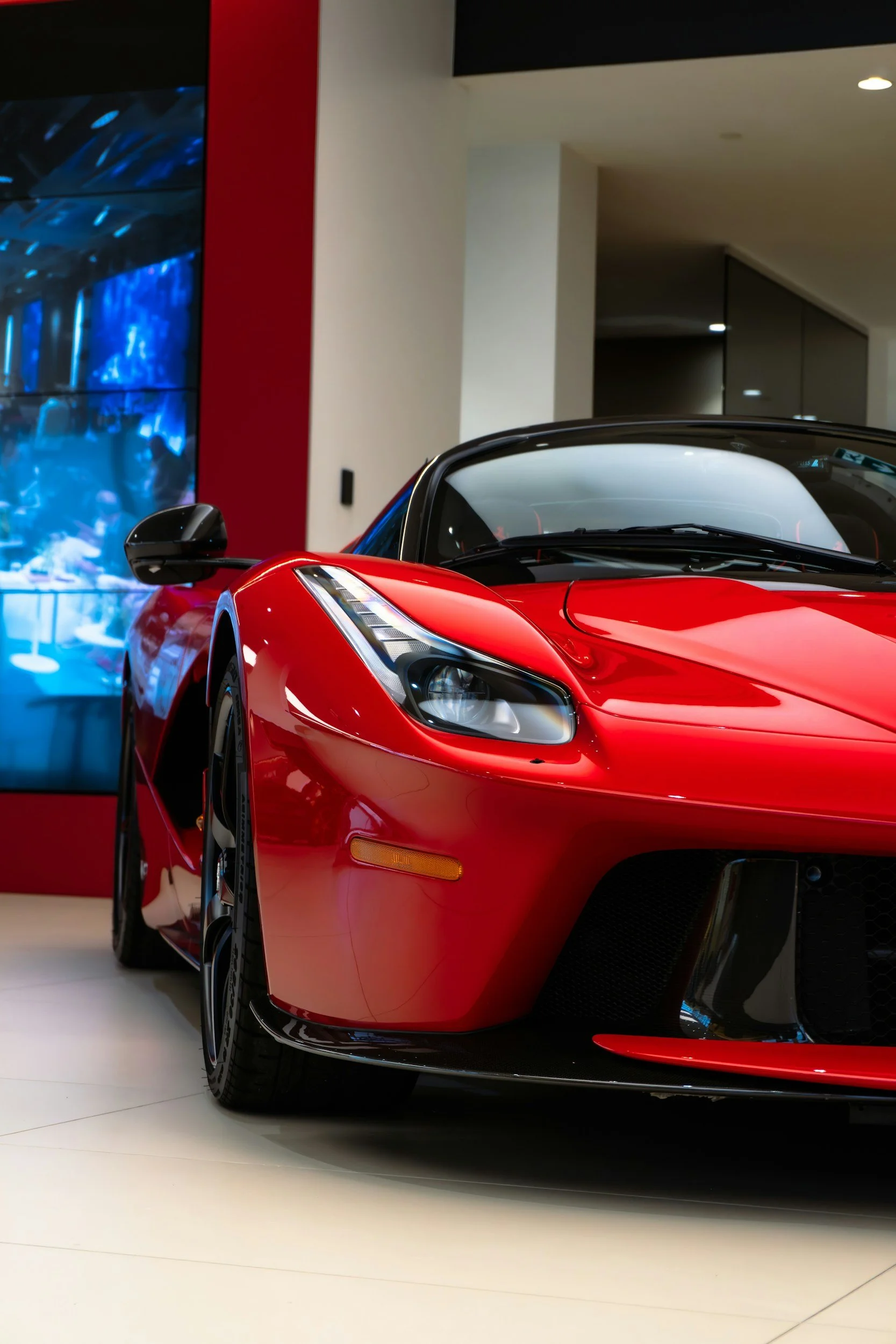 Red sports car displayed indoors, with a black roof, black wheels, and sleek design, parked near a red vending machine or display, in a modern showroom or dealership.