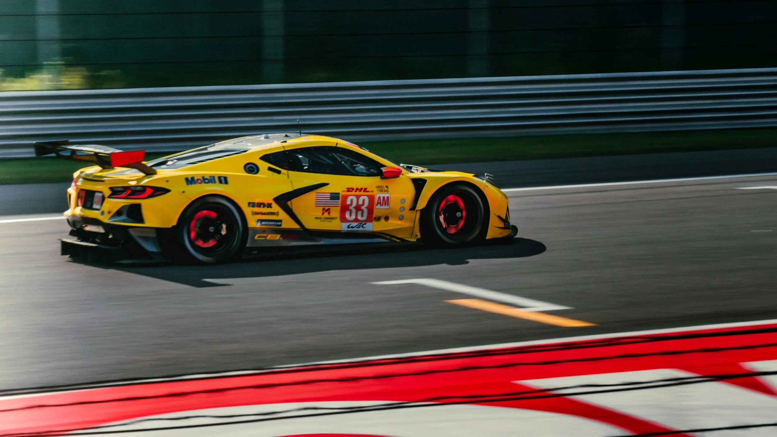Yellow race car with black and red accents speeding on a racetrack with blurred background.