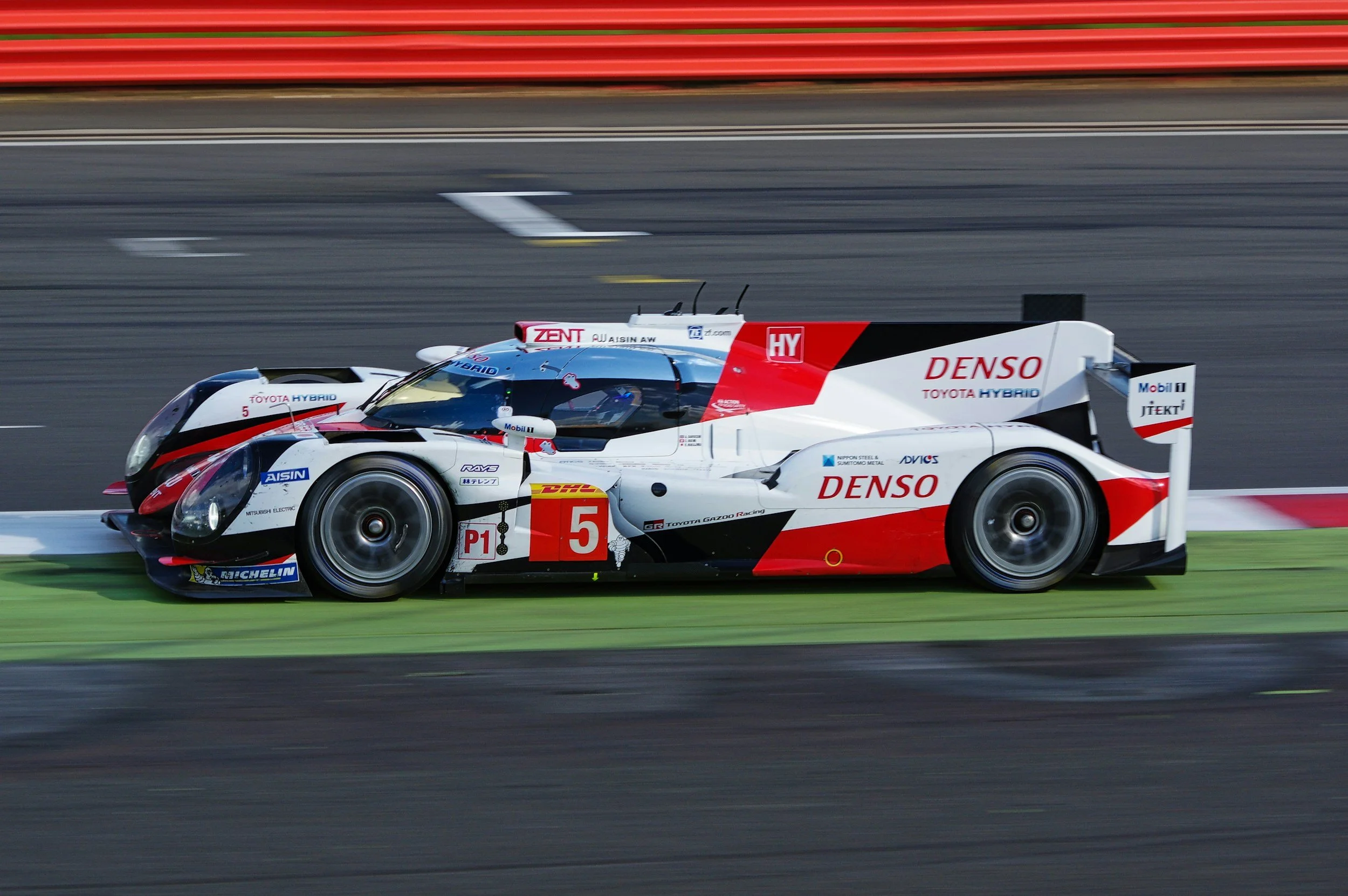 A Toyota hybrid racing car speeds along a track with a blurred background.