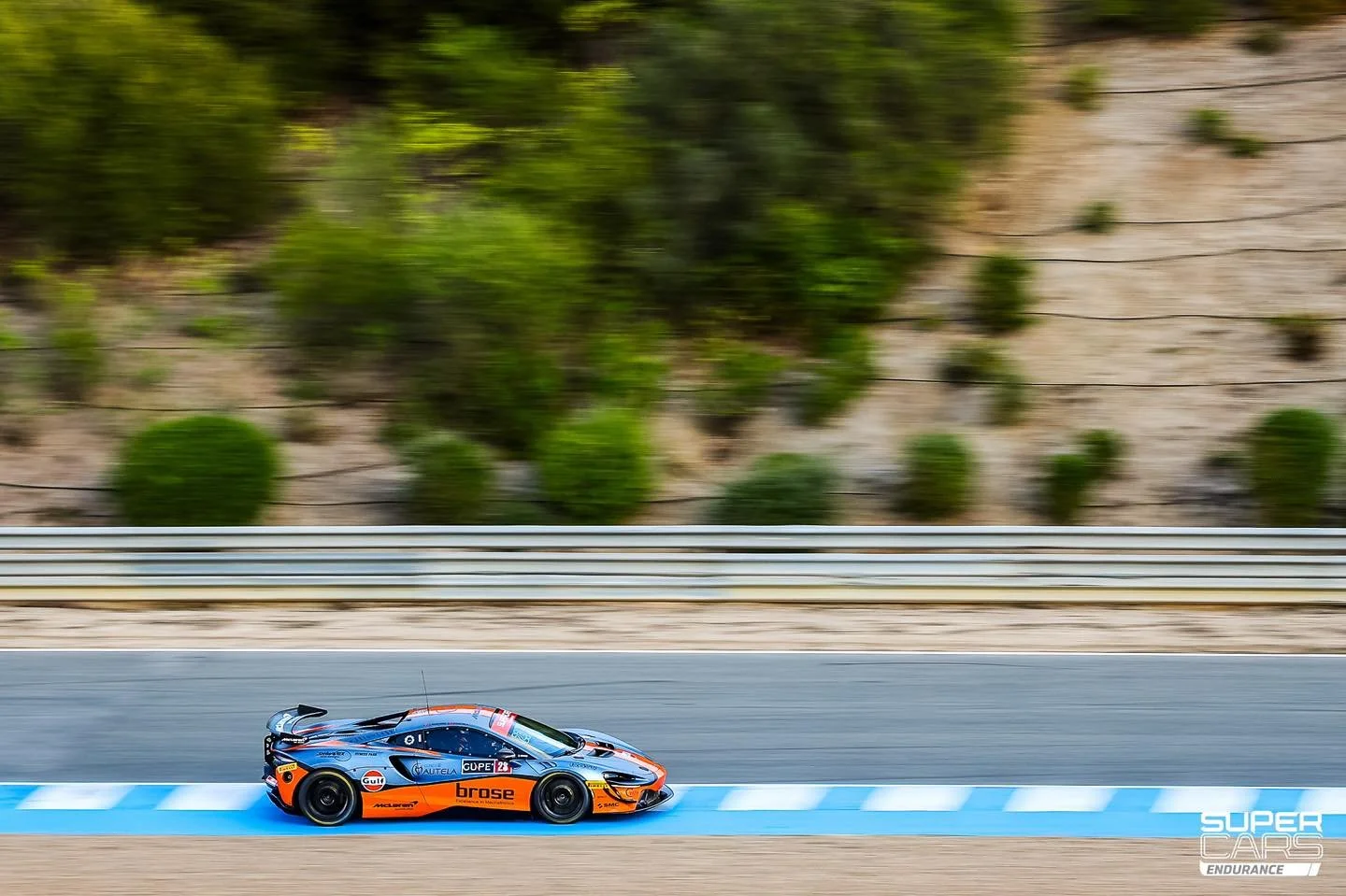 A race car on a track with a landscape of trees and hills in the background