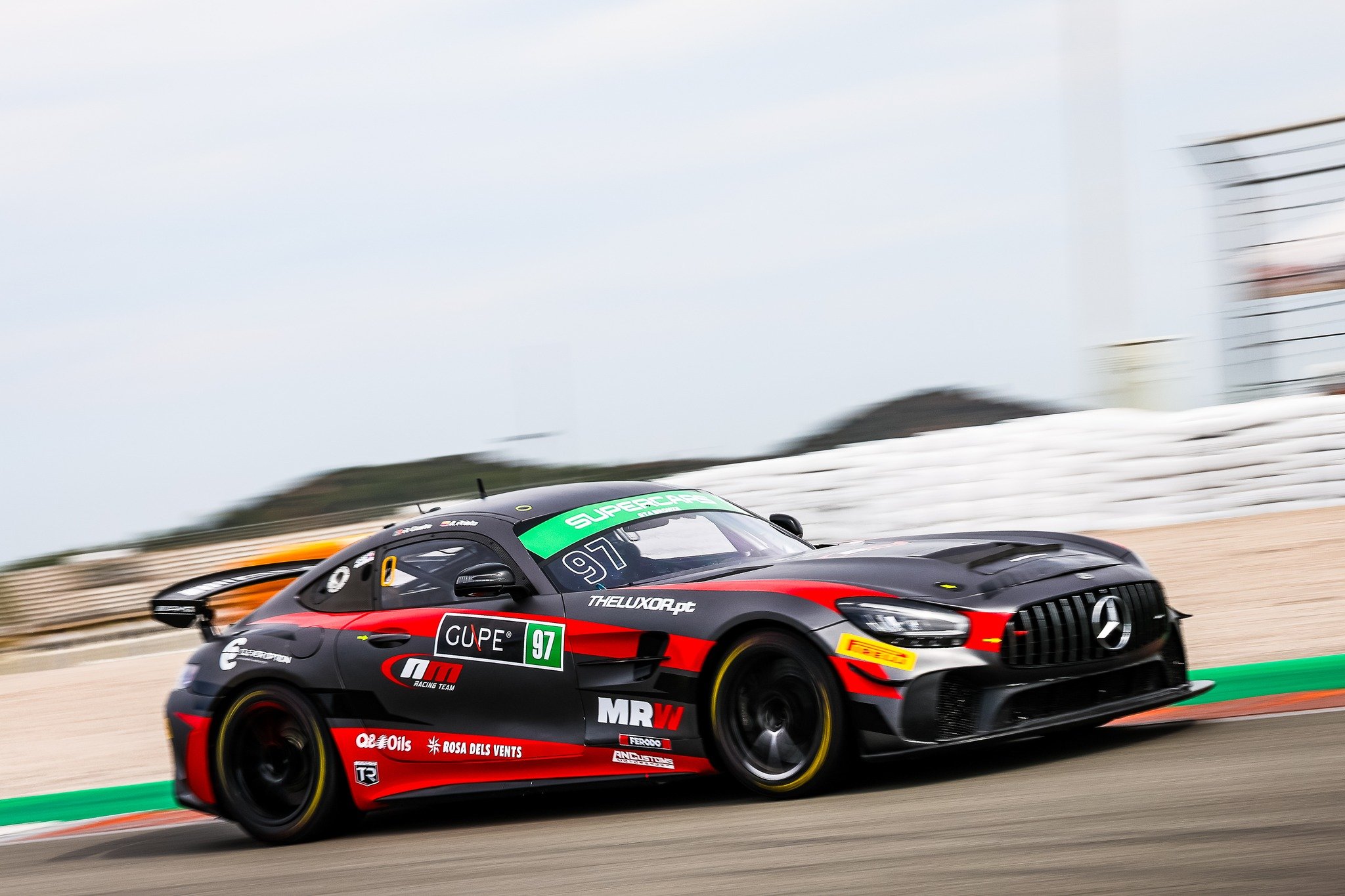 Black and red race car with Mercedes logo on track, moving swiftly with blurred background.