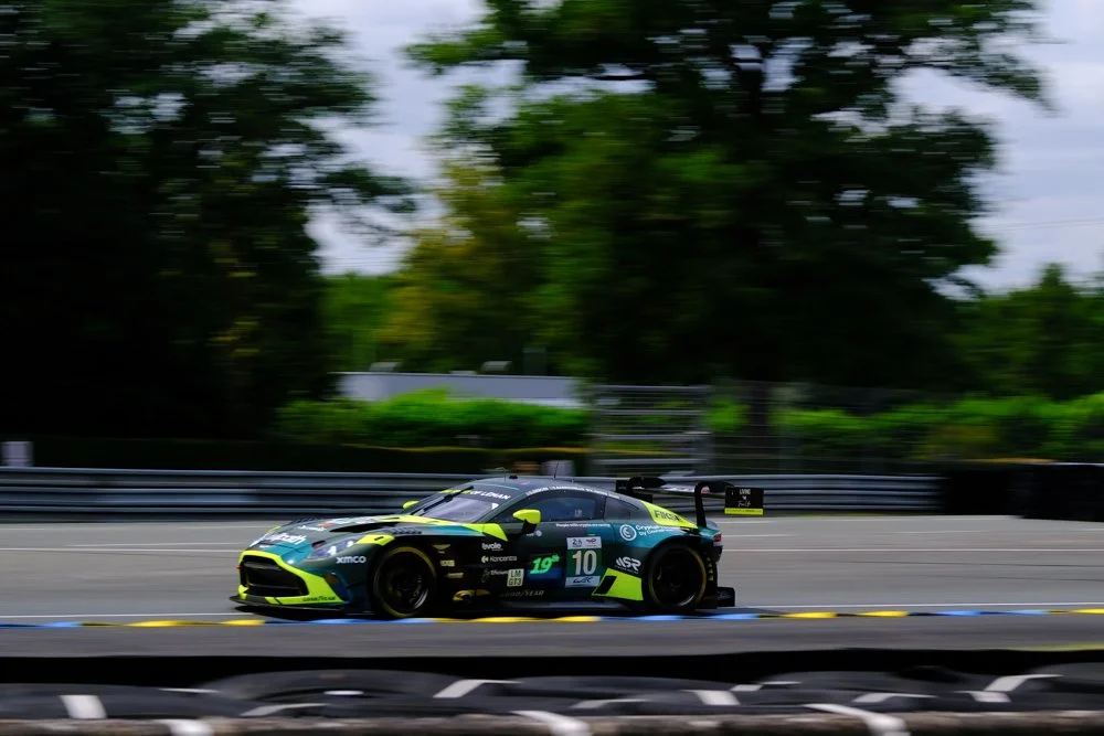 A race car speeding on a track with blurred background of trees and barriers.