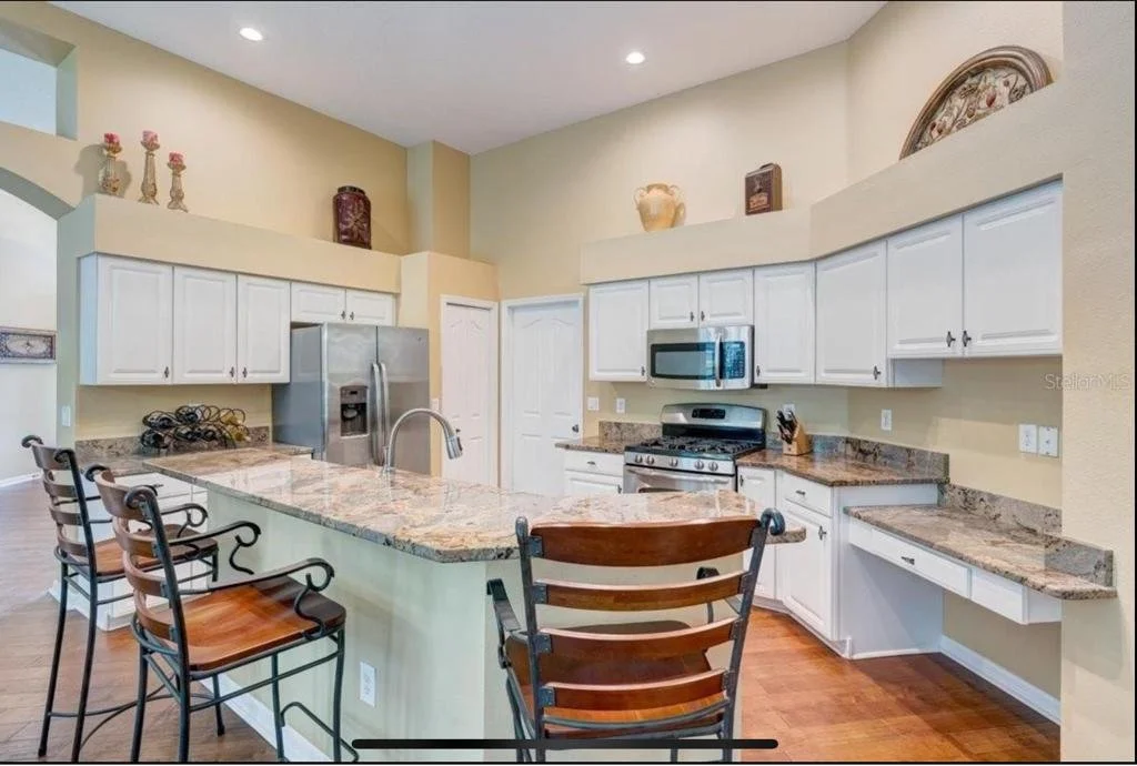 Before photo of a Sarasota kitchen with dated brown granite countertops, wood floors, and white cabinets before upgrading to a marble look porcelain countertop.