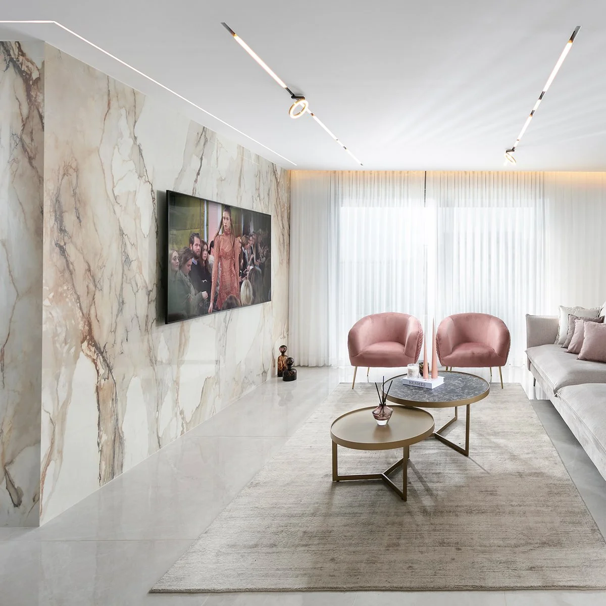 A modern glam living room featuring a seamless bookmatched Calacatta Antique porcelain feature wall behind a minimalist coffee table.