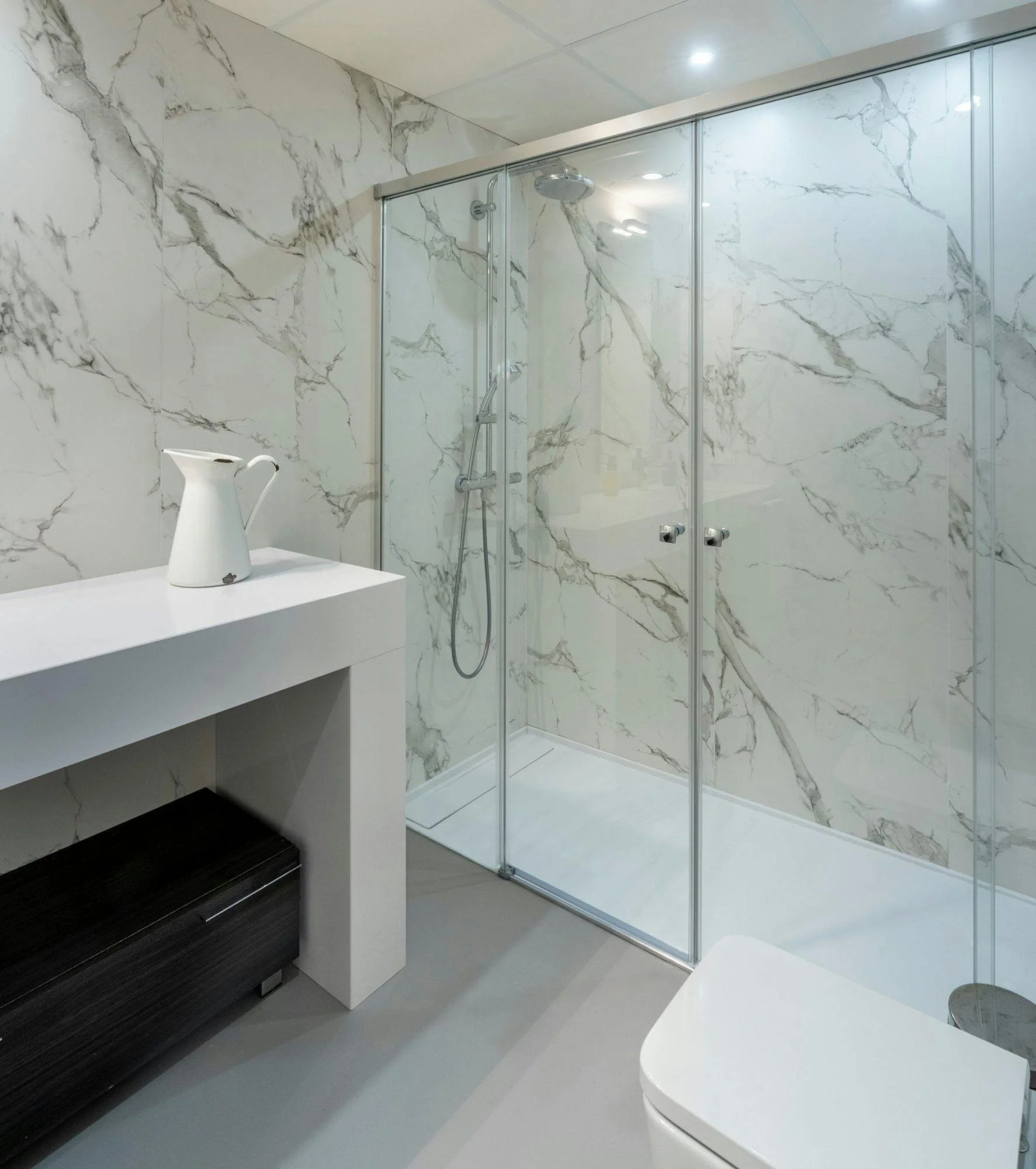 A luxury walk-in bathroom comparing Dekton vs Quartz for shower walls, showing large format seamless slabs with zero grout lines.