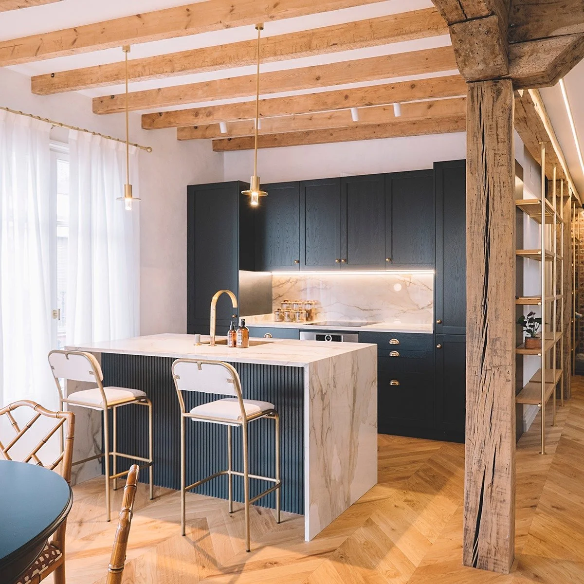 A modern farmhouse kitchen showcasing marble look porcelain countertops and a matching full-height backsplash with warm wood beams overhead.
