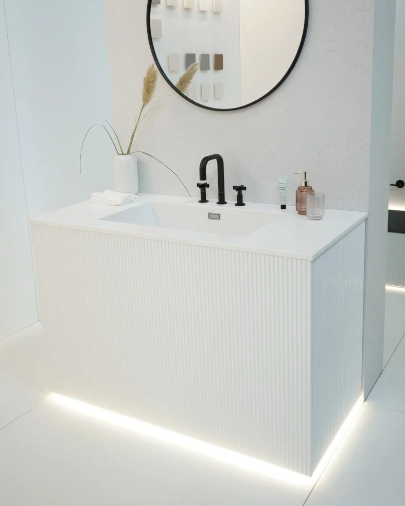 Modern bathroom vanity with a round mirror, a black faucet, beige plant decor, and grooming products on the counter.