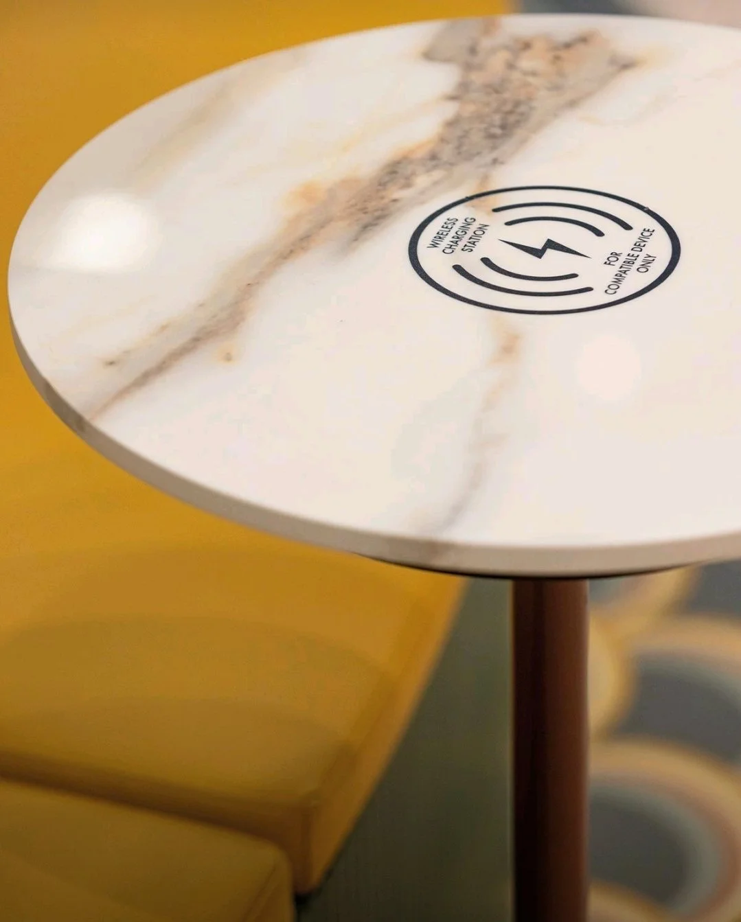 Integrated wireless charging module installed beneath a 4D porcelain table top with marble veining, showing the laser-etched charging icon for a cord-free hospitality experience.