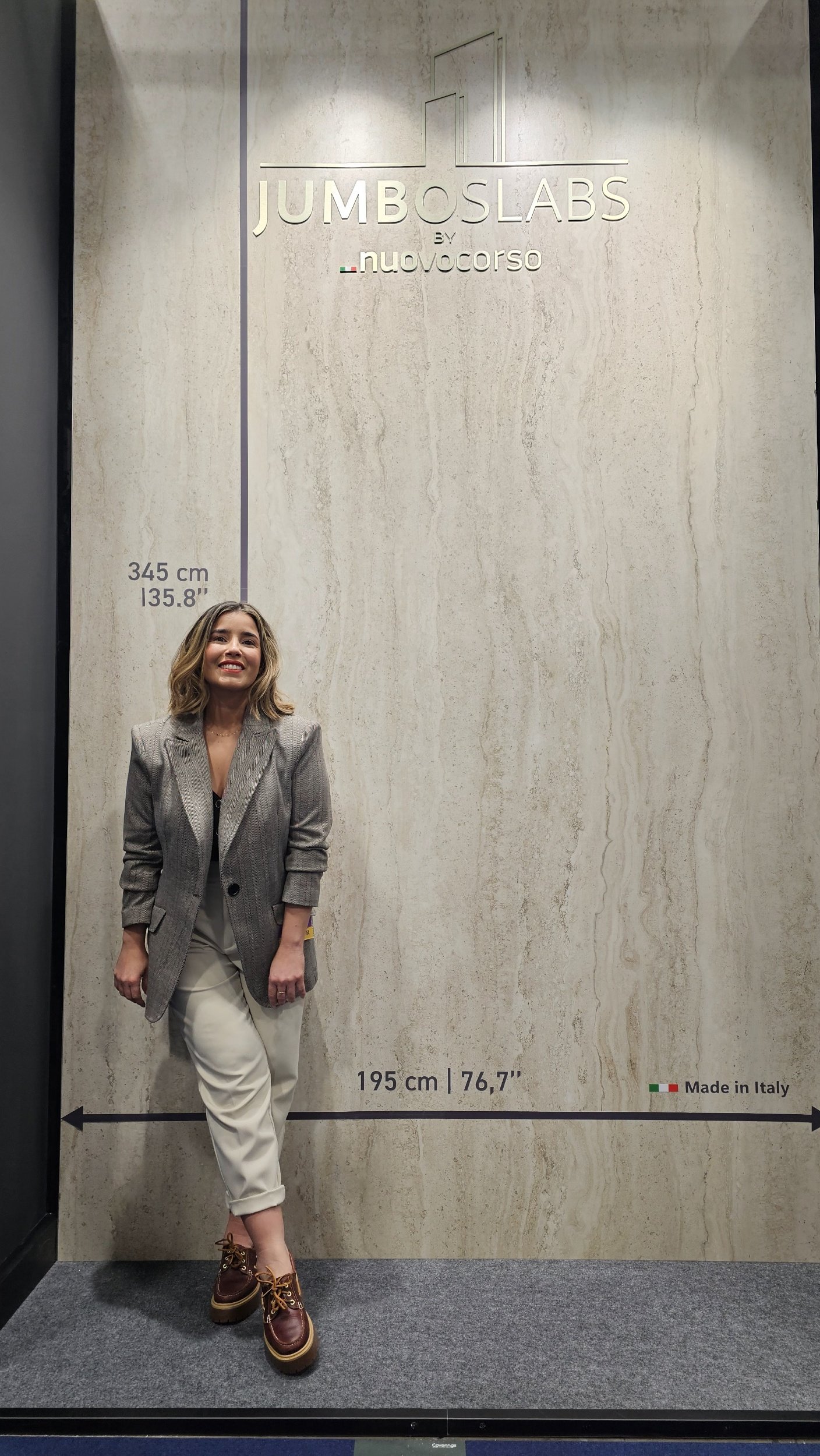Expert Lais Luz standing next to a massive, made-in-Italy porcelain slab displaying jumbo-format dimensions of 195 cm (76.7") by 345 cm (135.8").