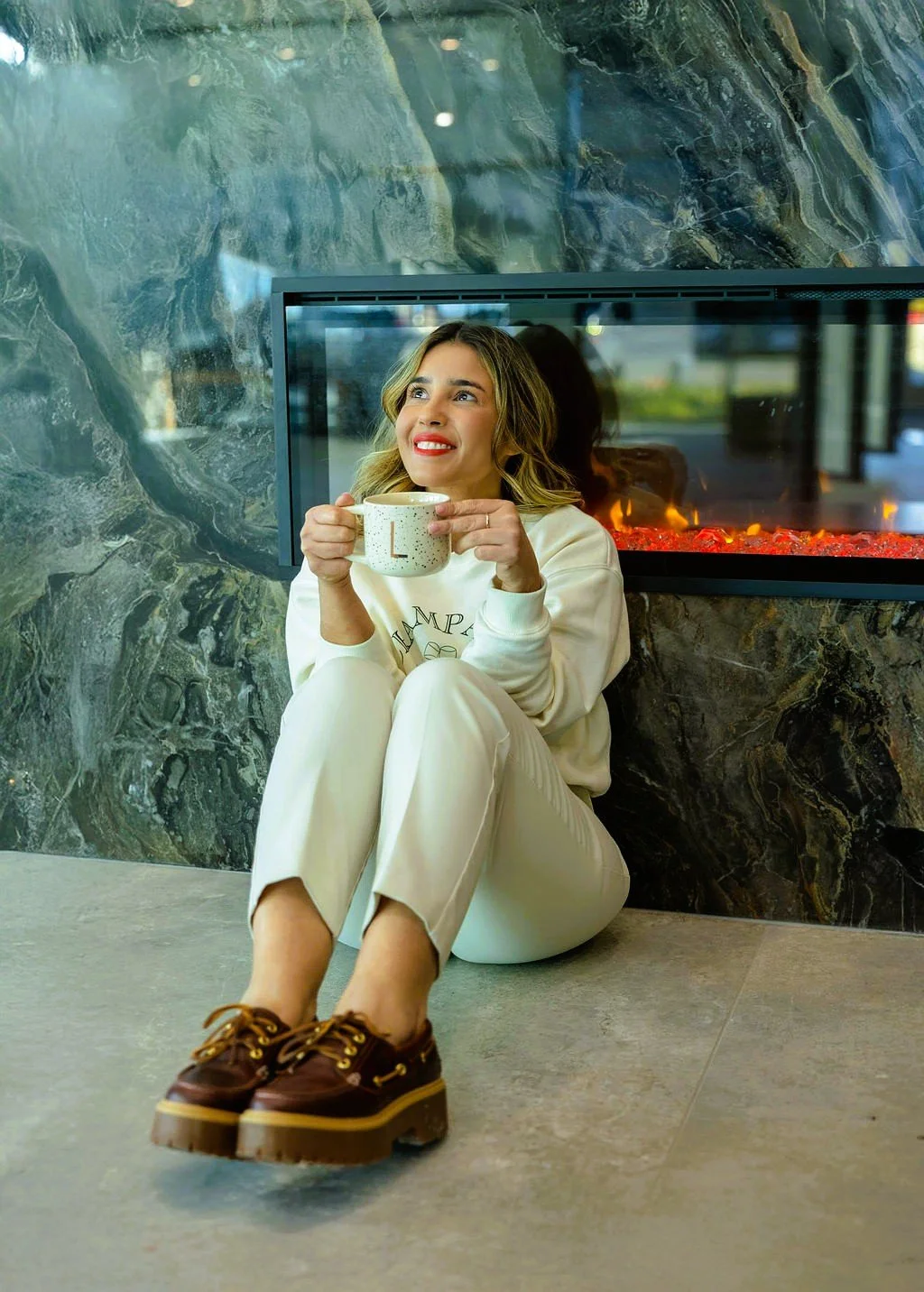 Lais Luz sitting in front of a luxury dark porcelain fireplace wall, enjoying the warmth of the electric fireplace insert.