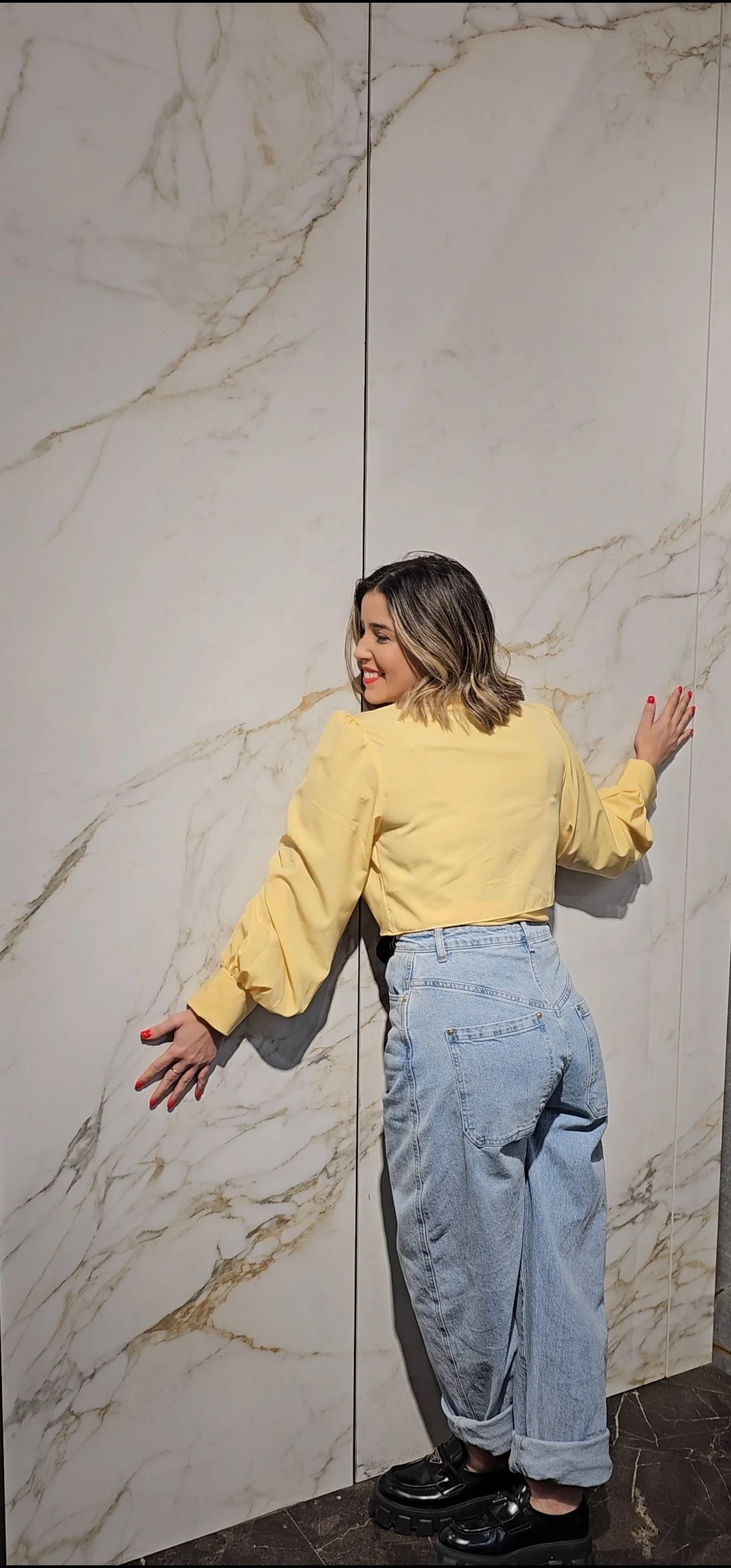 Fabrication expert Lais Luz hugging a massive integrated pivot entrance door clad in bookmatched Calacatta-pattern porcelain slabs, celebrating the seamless, high-performance execution.