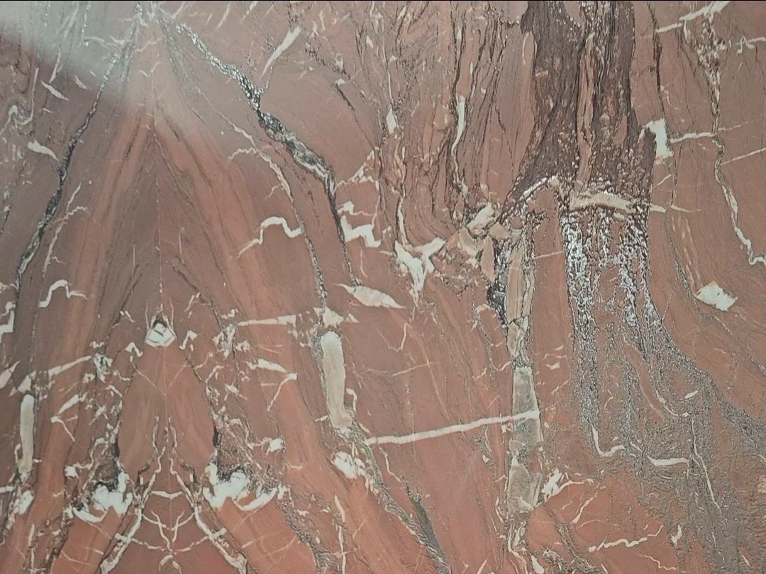 Close-up of Rosso Cardinale porcelain slab showcasing the intricate bookmatched veining in earthy red, white, and charcoal tones.