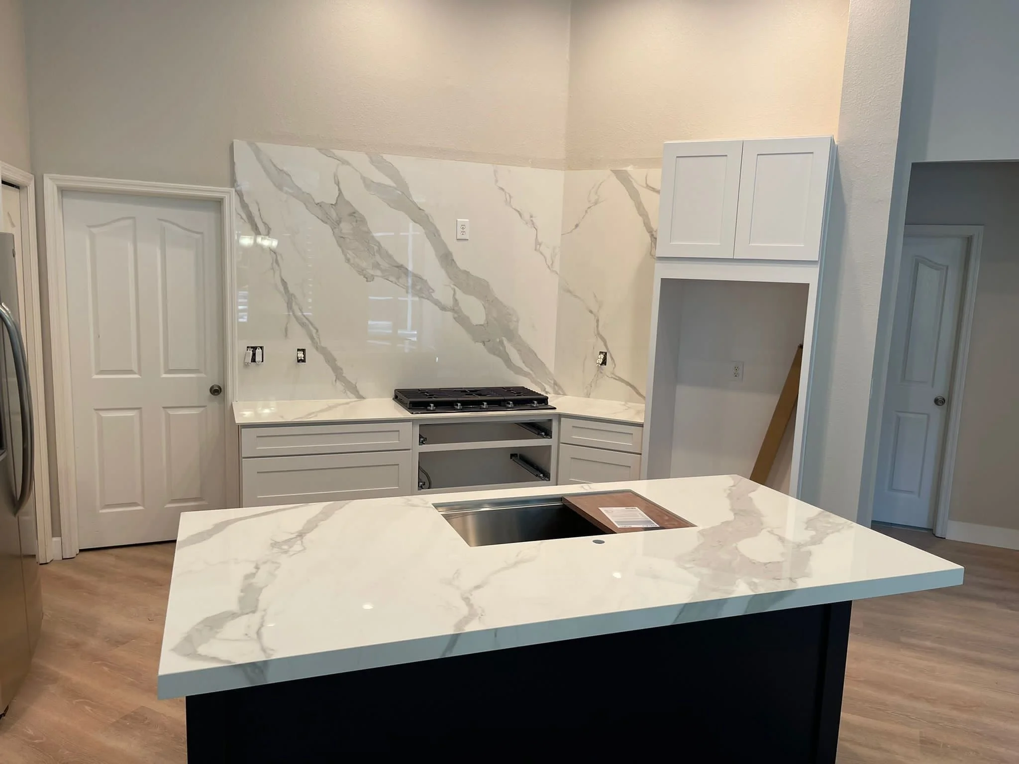 Installation progress of Infinity Classic Statuario porcelain countertops and a matching full height slab backsplash before the range hood and shelving are added.