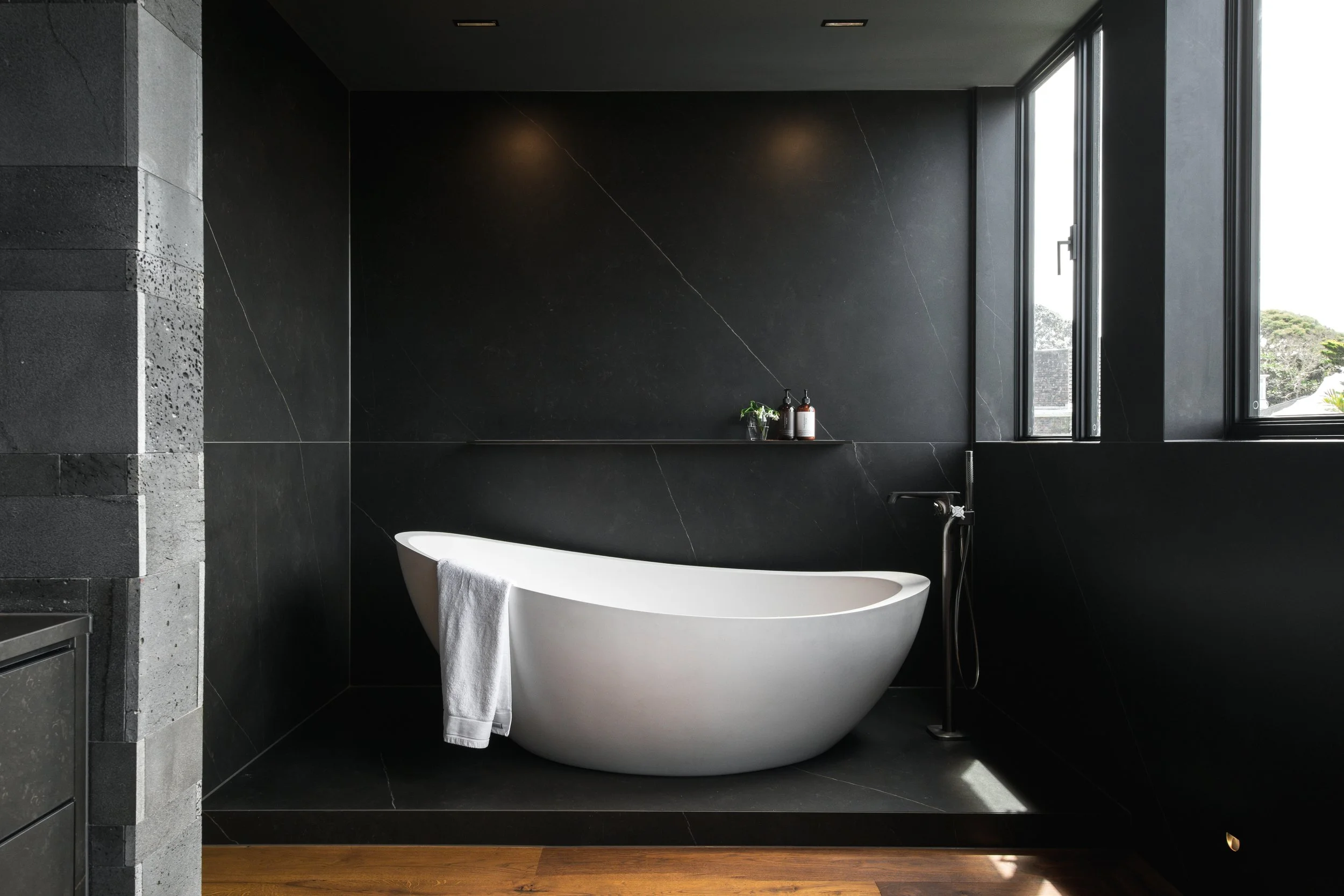 The dark, rich tones create a striking contrast against the crisp white tub, while the seamless walls and integrated shelf enhance the modern aesthetic.