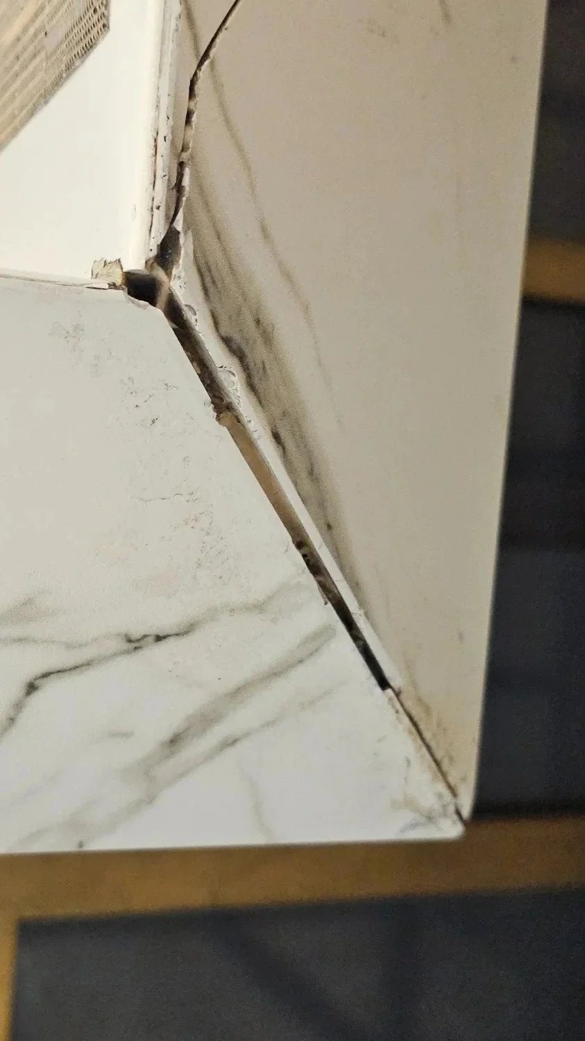 Failed porcelain slab mitered edge installation showing cracking and improper bonding due to non-specialist fabrication.