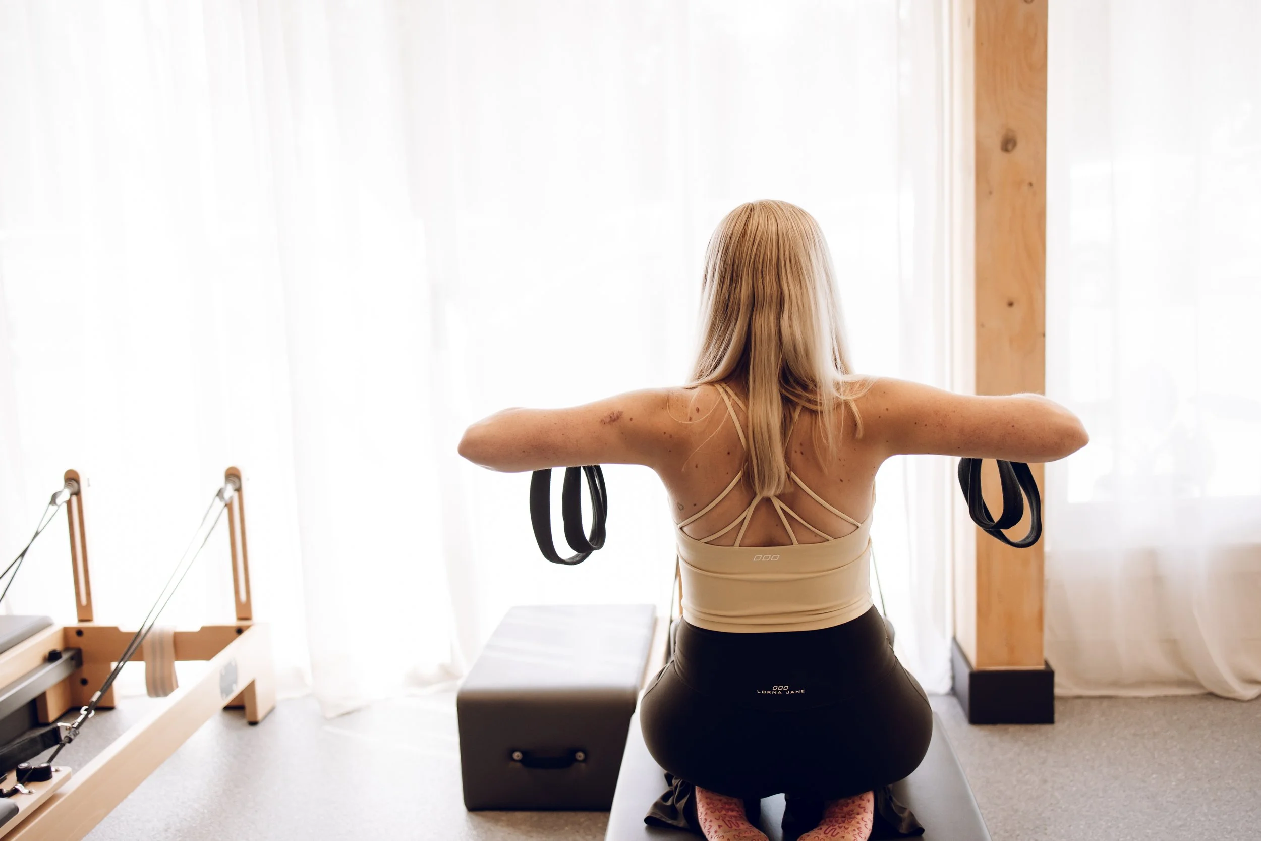 Instructor leading a fitness class with women using resistance bands on Pilates reformers in a modern studio.