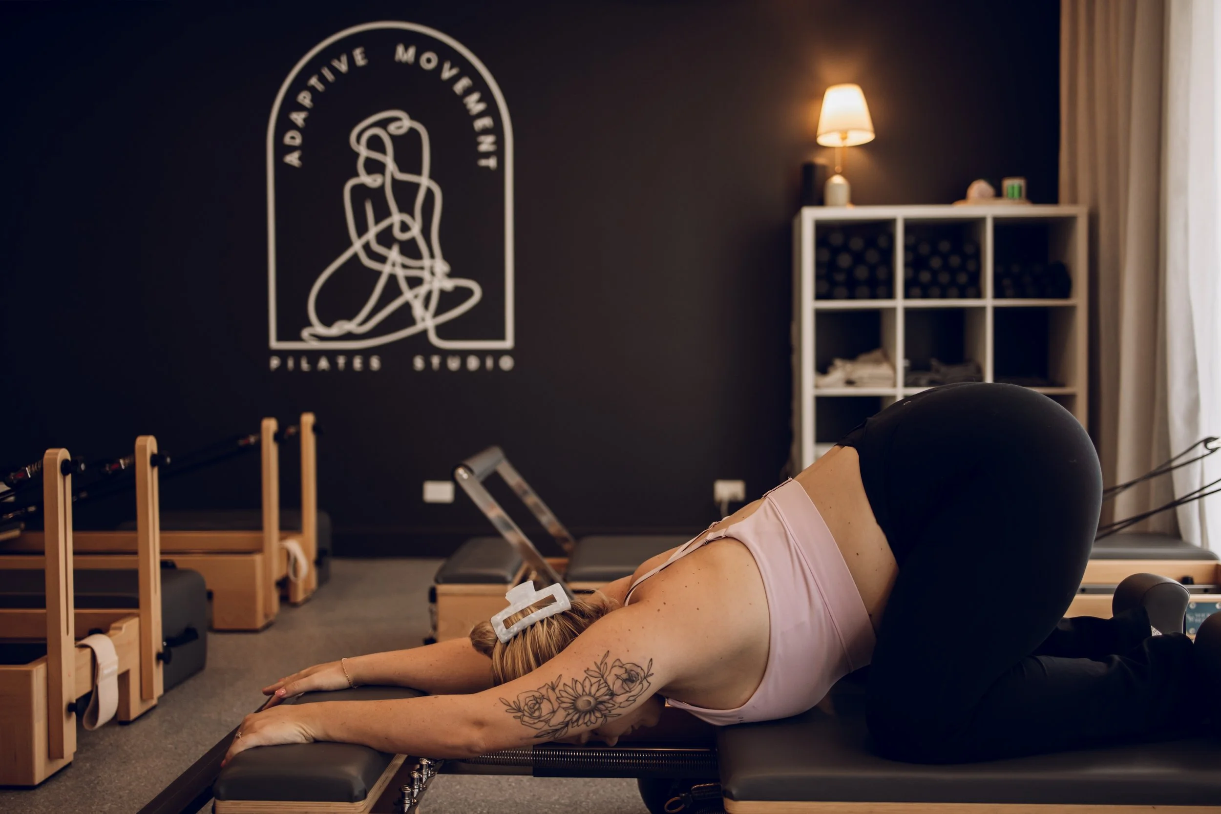 A woman practicing yoga on a reformer machine in a Pilates studio.