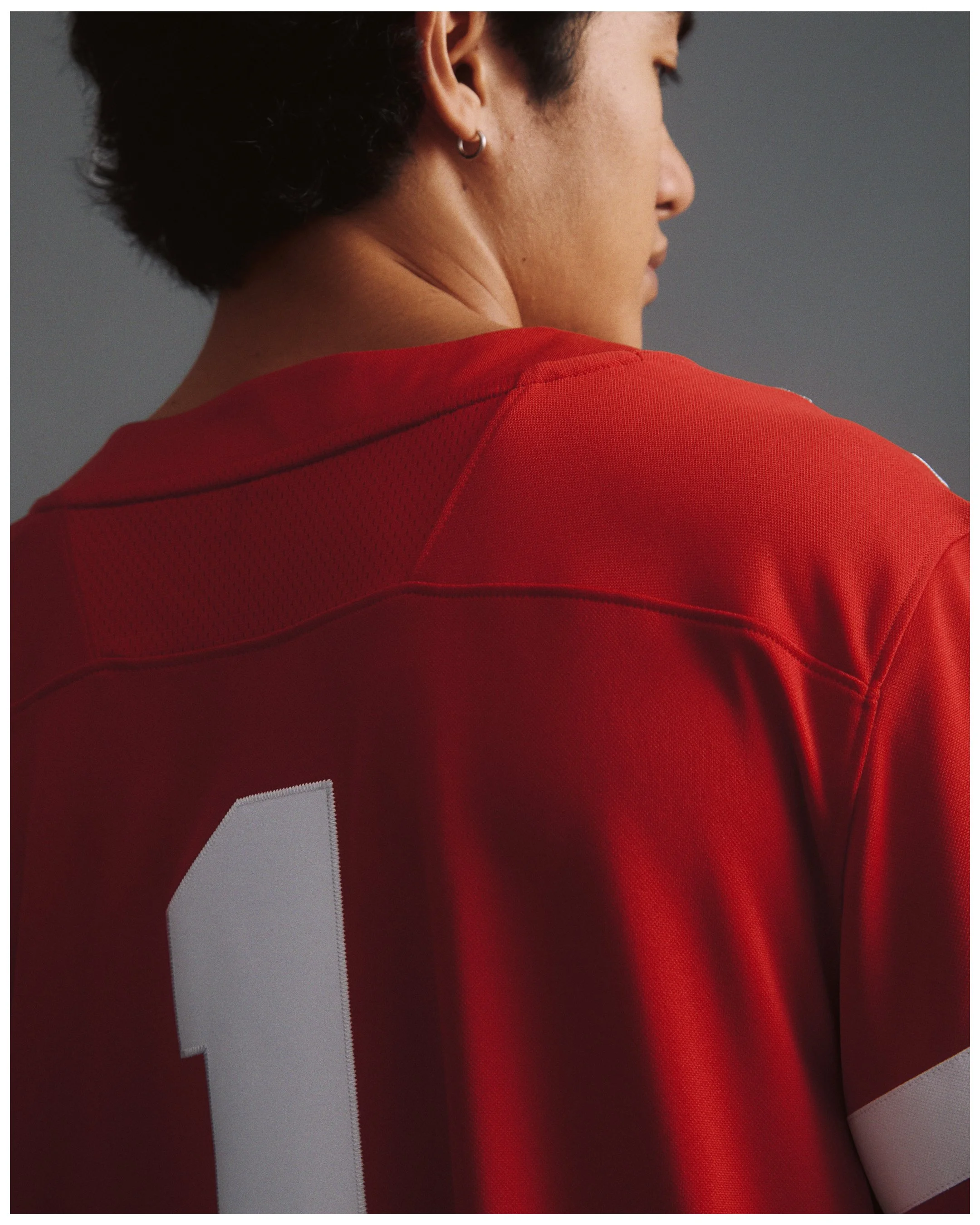 A person wearing a red sports jersey with a large white number on the back, viewed from the side and slightly behind.