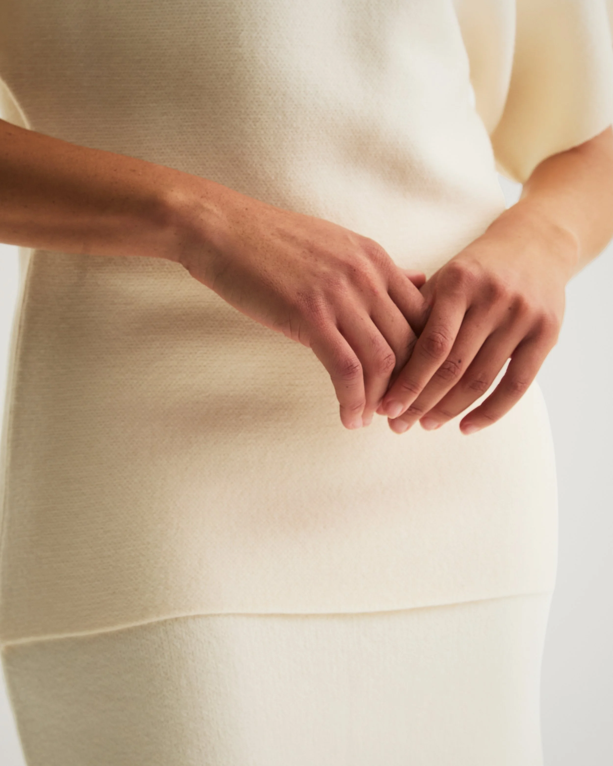 Close-up of a person's hands clasped together, wearing a cream-colored dress or top.