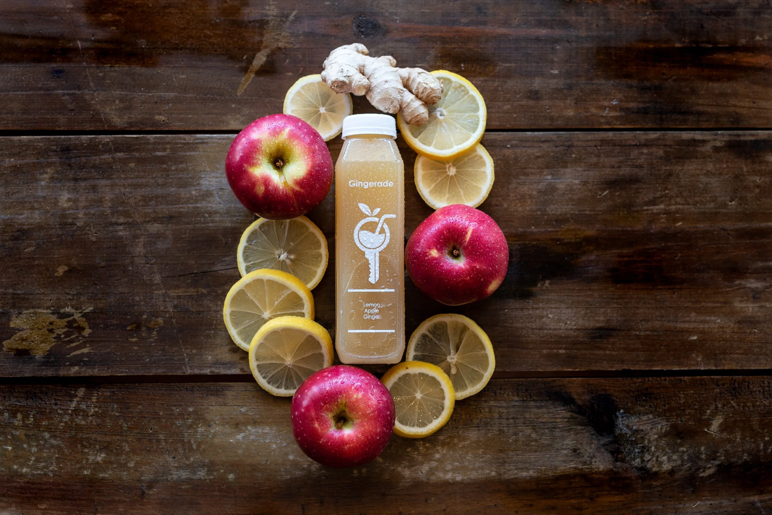 Lemon, apple, and ginger slices arranged around a gingerade juice bottle on a wooden surface. Photo by Brock Byers 