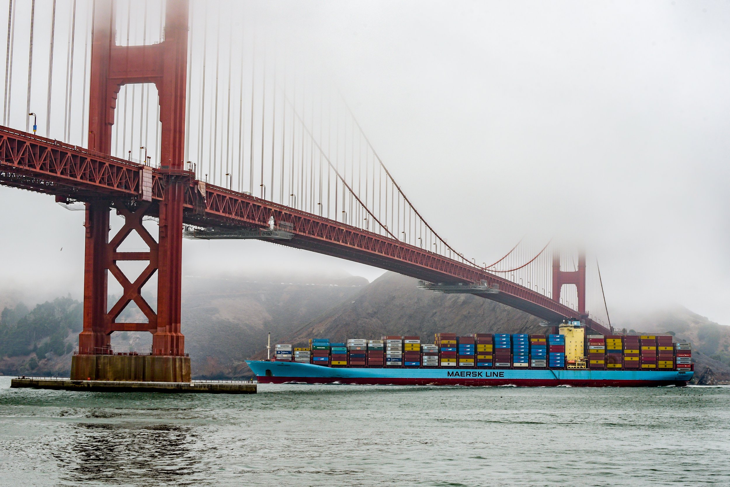 A cargo ship labeled 'Maersk Line' passing under the Golden Gate Bridge on a foggy day. Photo by Brock Byers 