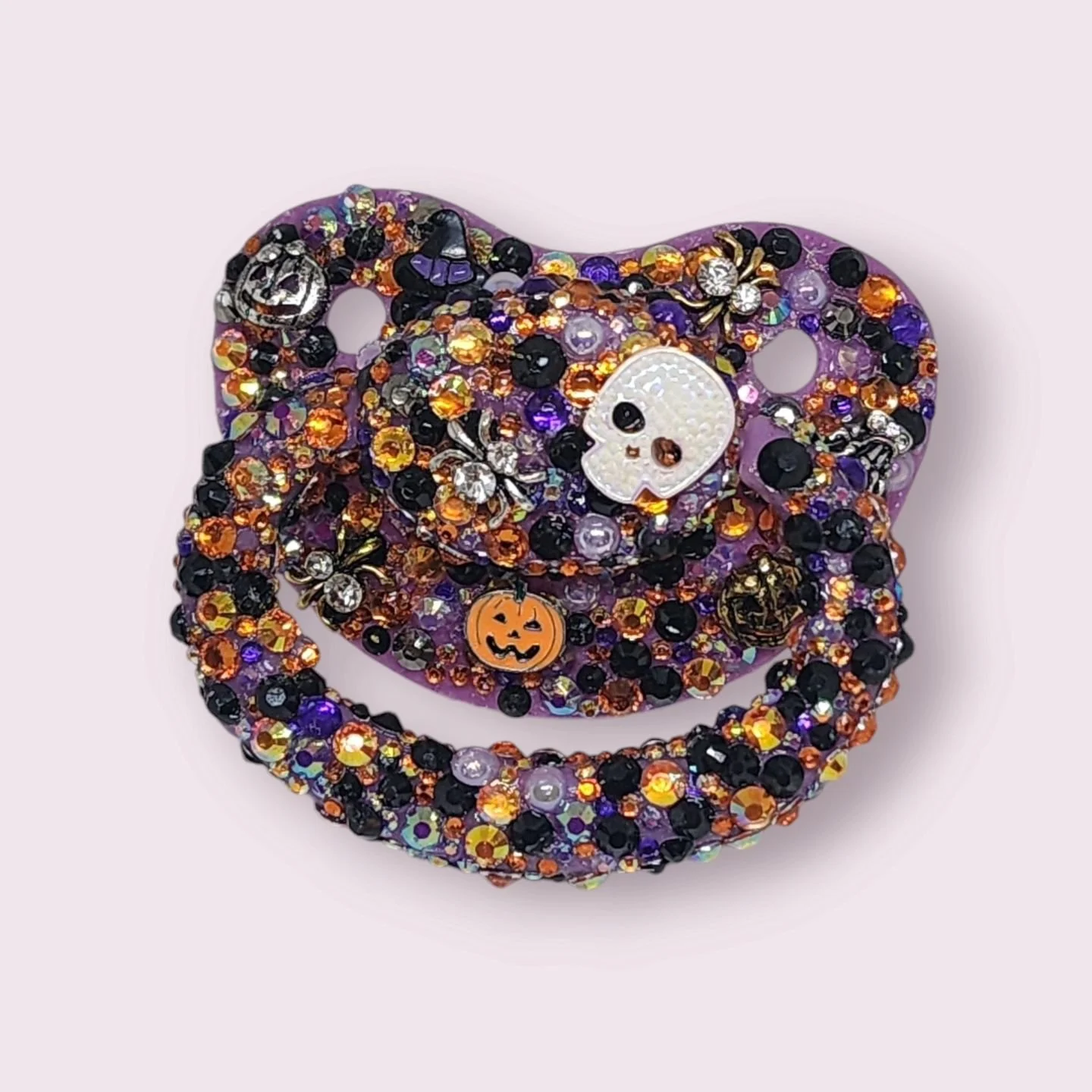 👻 Spooky season may be over, but our *Haunted Halloween Paci* is still here and now on SALE for just $10! 🎃✨ Decorated with spiders, skeletons, skulls, and carved pumpkins, this orange, purple, and black paci is perfect for anyone who loves a bit o