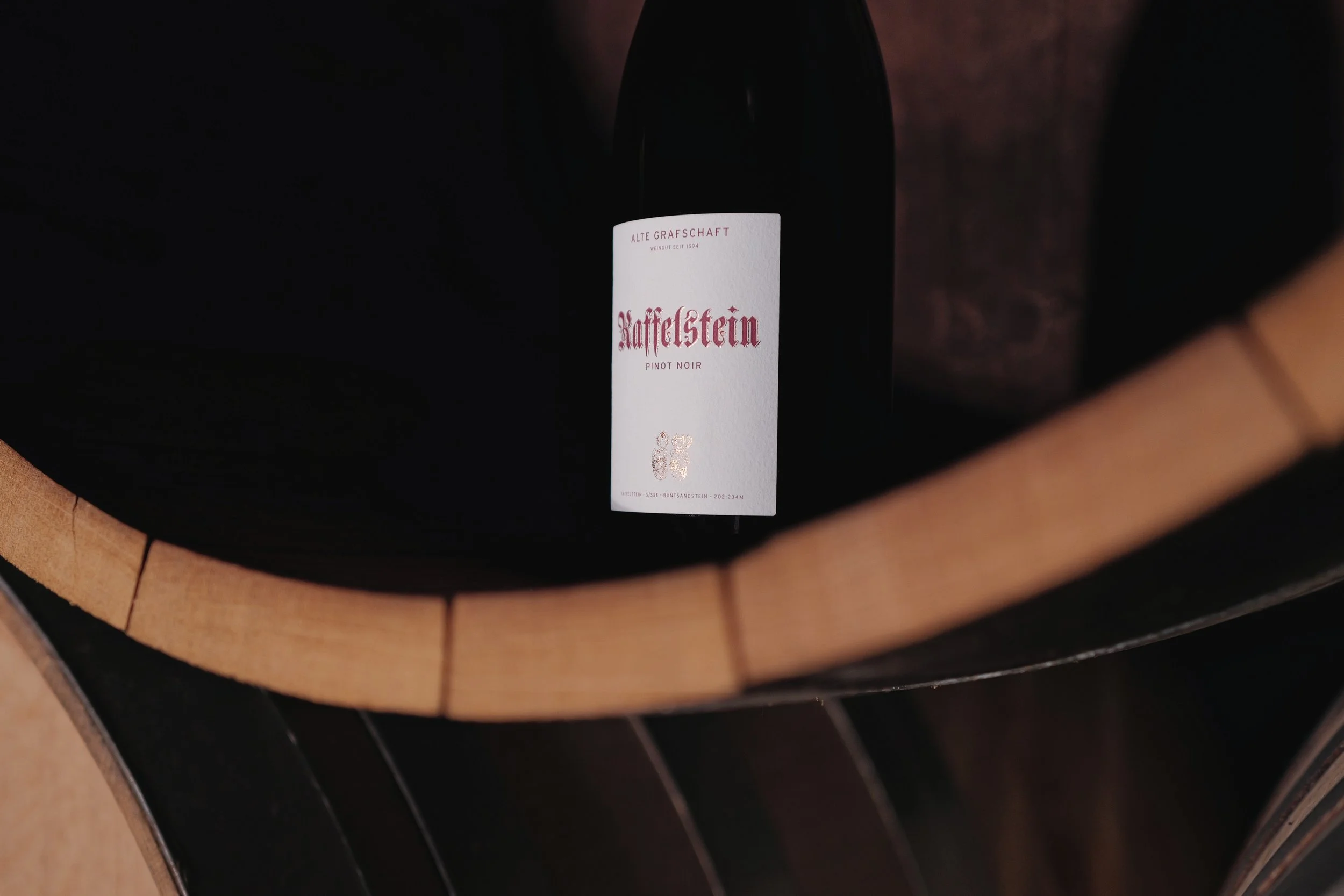 Eine Flasche Wein auf einem Holzfass, das im Keller steht.