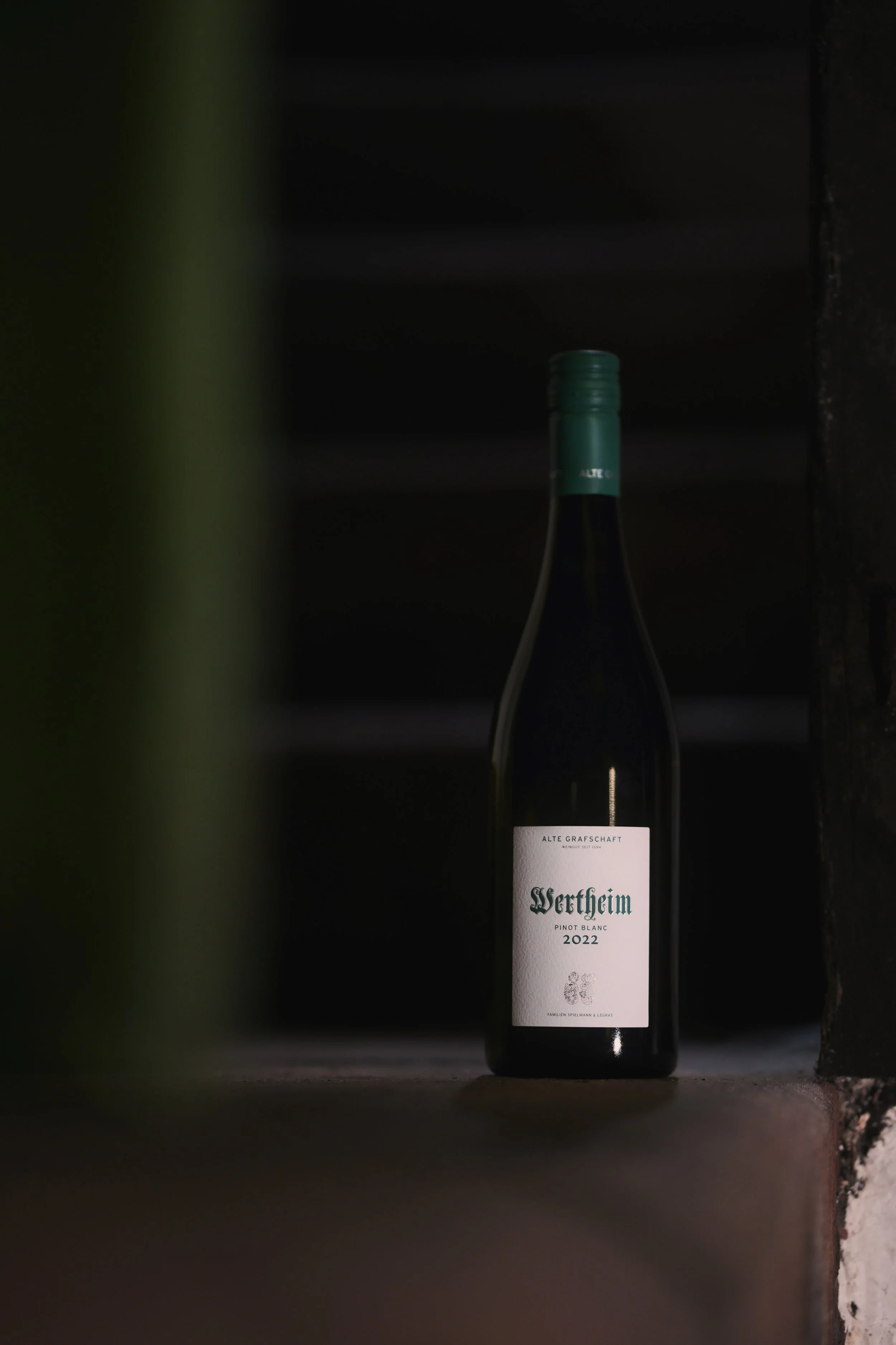 Eine Flasche Wein mit weißem Etikett, das 'Wertheim Pinot Blanc 2022' schreibt, befindet sich in einer dunklen Umgebung.