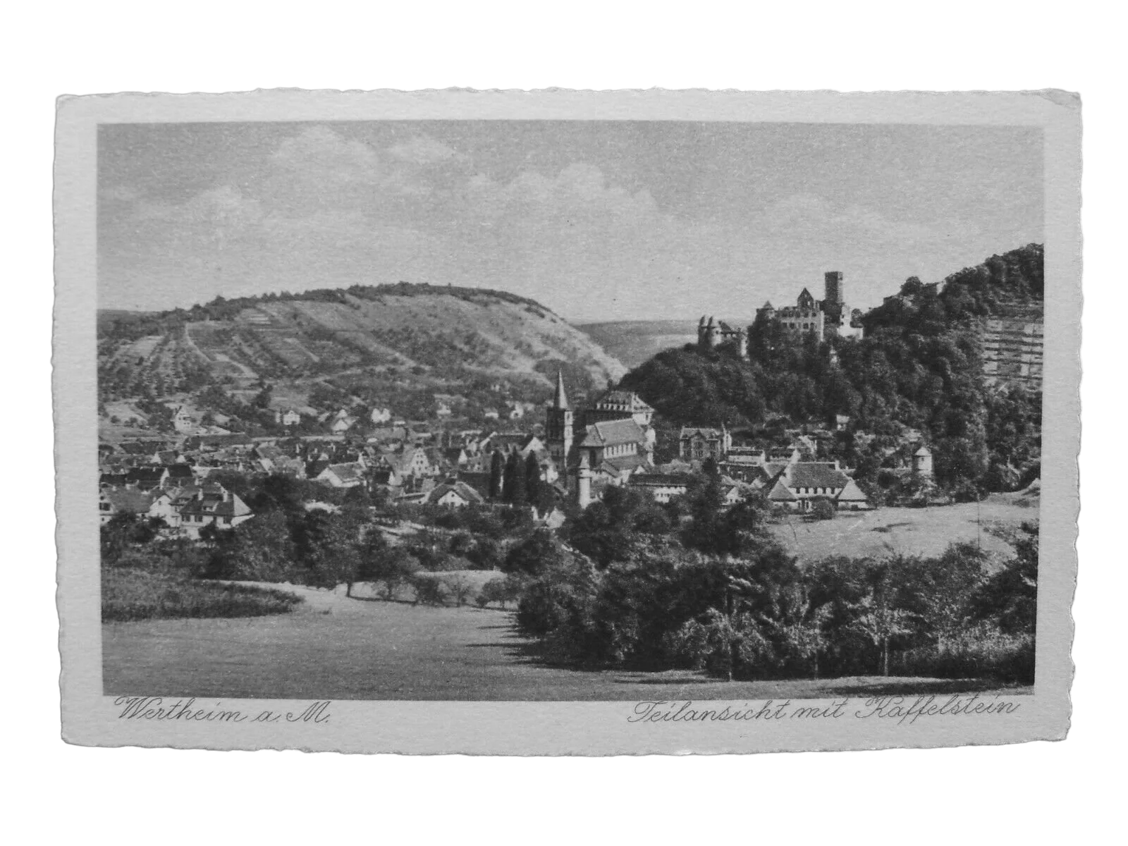 Schwarz-Weiß-Fotografie eines Dorfes mit Kirche und Schloss auf einem Hügel, umgeben von Feldern und Bäumen. Text darunter: "Wertheim a. M." und "Teilansicht mit Kaffelstein".