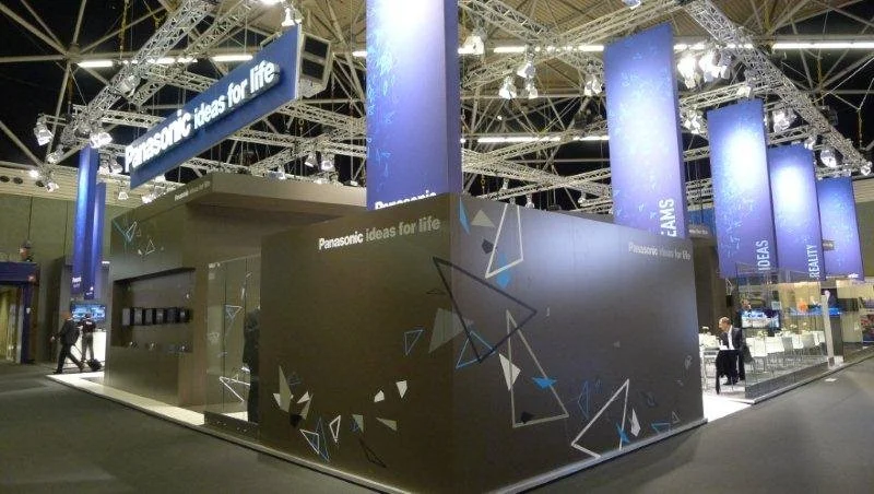 Übersicht des dunkel gestalteten Panasonic Home-Entertainment-Messestands mit Kinofeeling, Dreiecksgrafik und blau beleuchteten Säulen