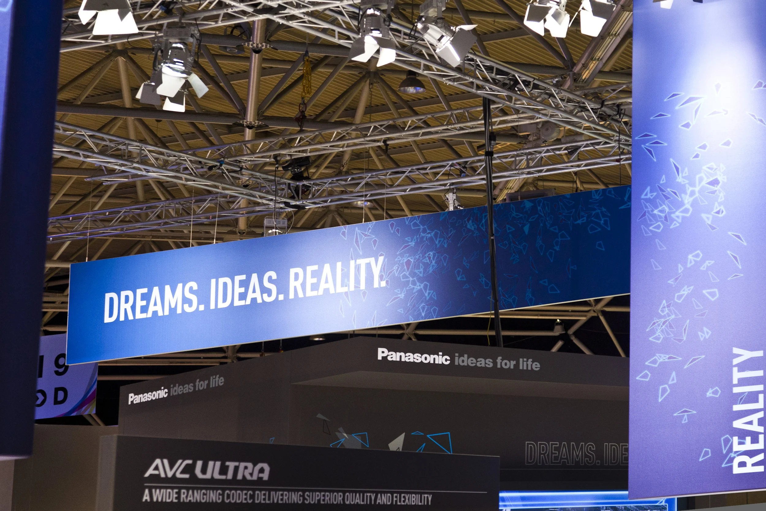 Panasonic Home-Entertainment-Messestand mit beleuchtetem „Dreams. Ideas. Reality."-Banner, Dreiecksgrafik und AVC-ULTRA-Produktkommunikation