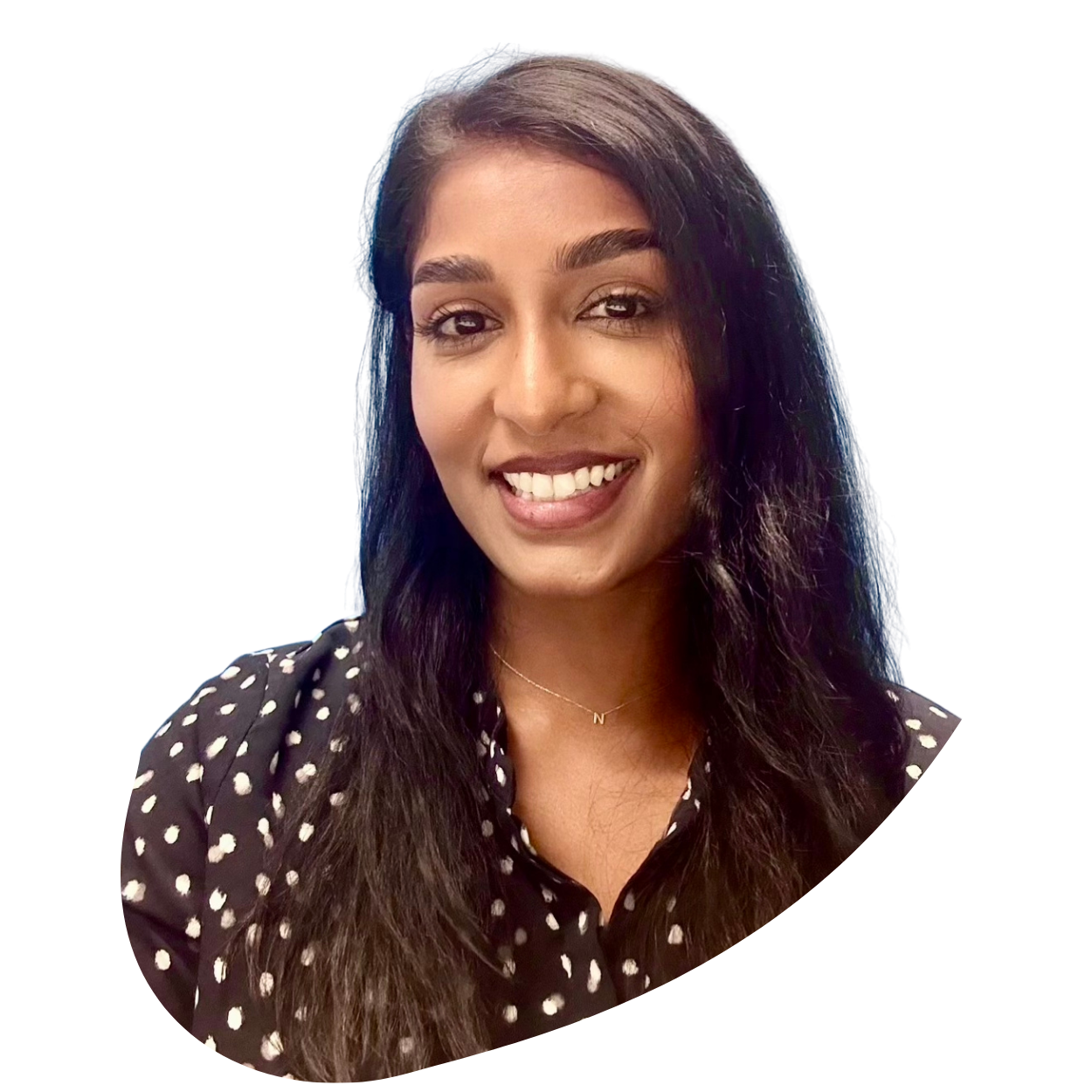 A smiling woman with long dark hair, wearing a black and white polka dot shirt and a delicate necklace with a small letter 'N' pendant.