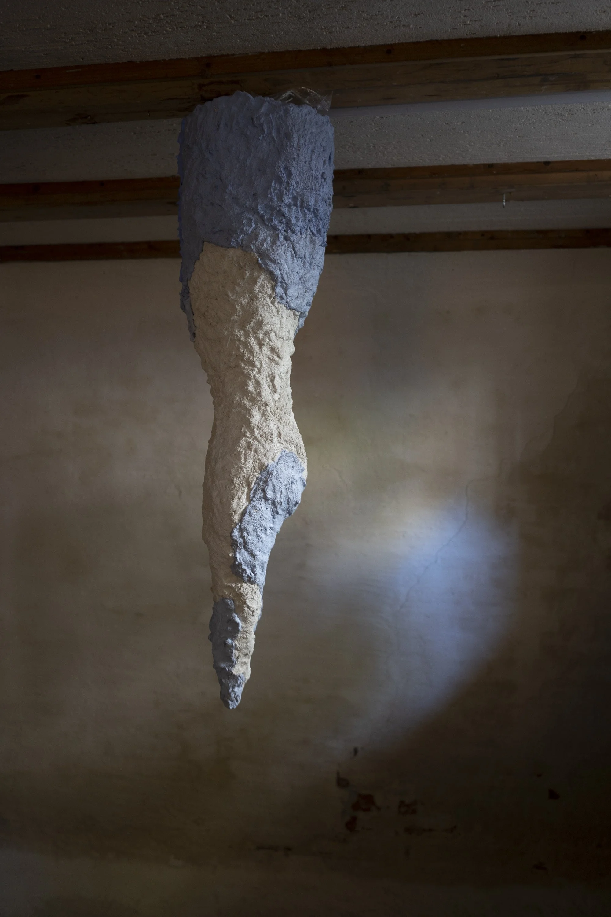 An abstract art sculpture hanging from the ceiling, made of textured, rough materials with a mix of cream and light blue colors.