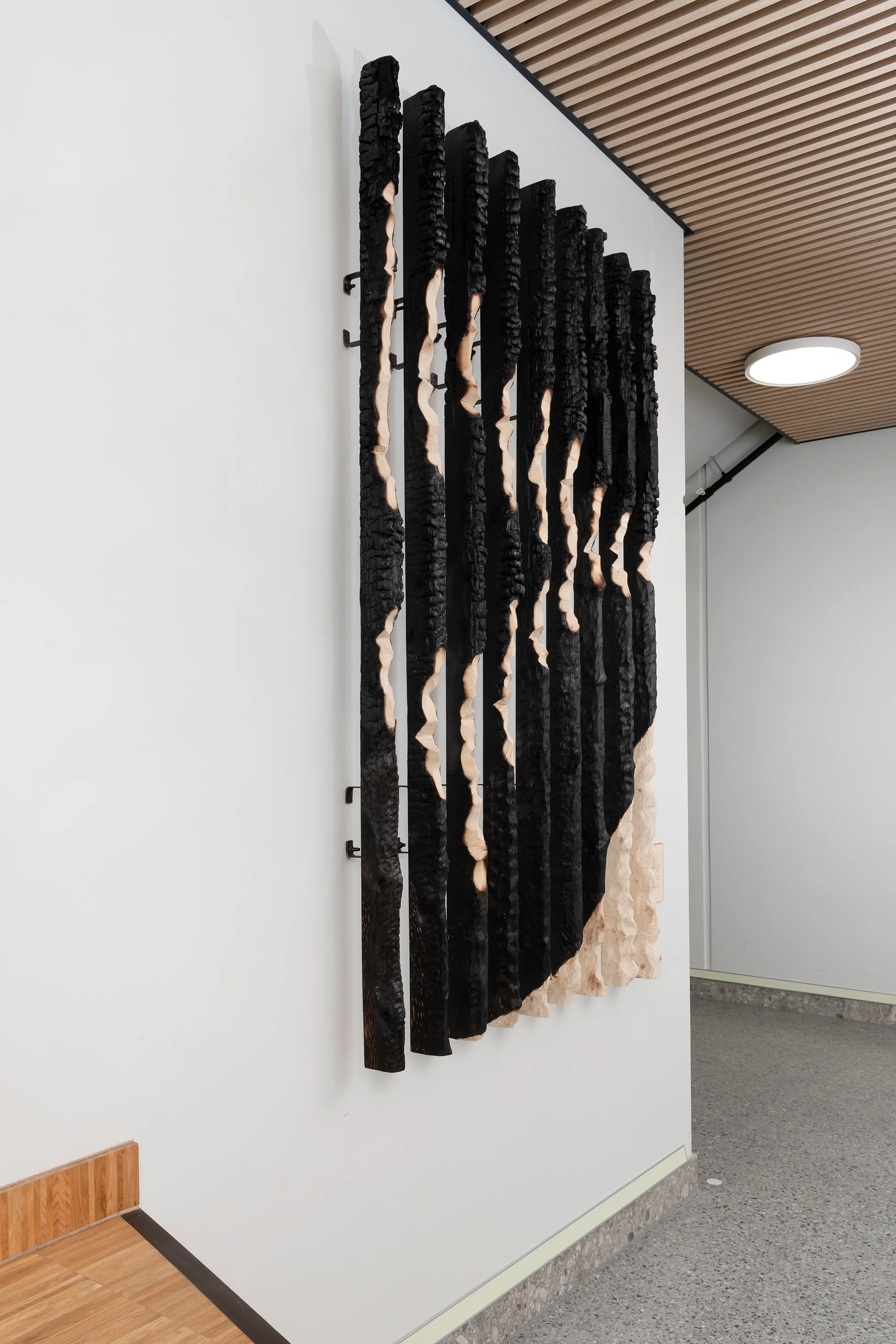 Wall-mounted abstract wooden sculpture with black and natural wood-colored vertical slats in a modern interior.