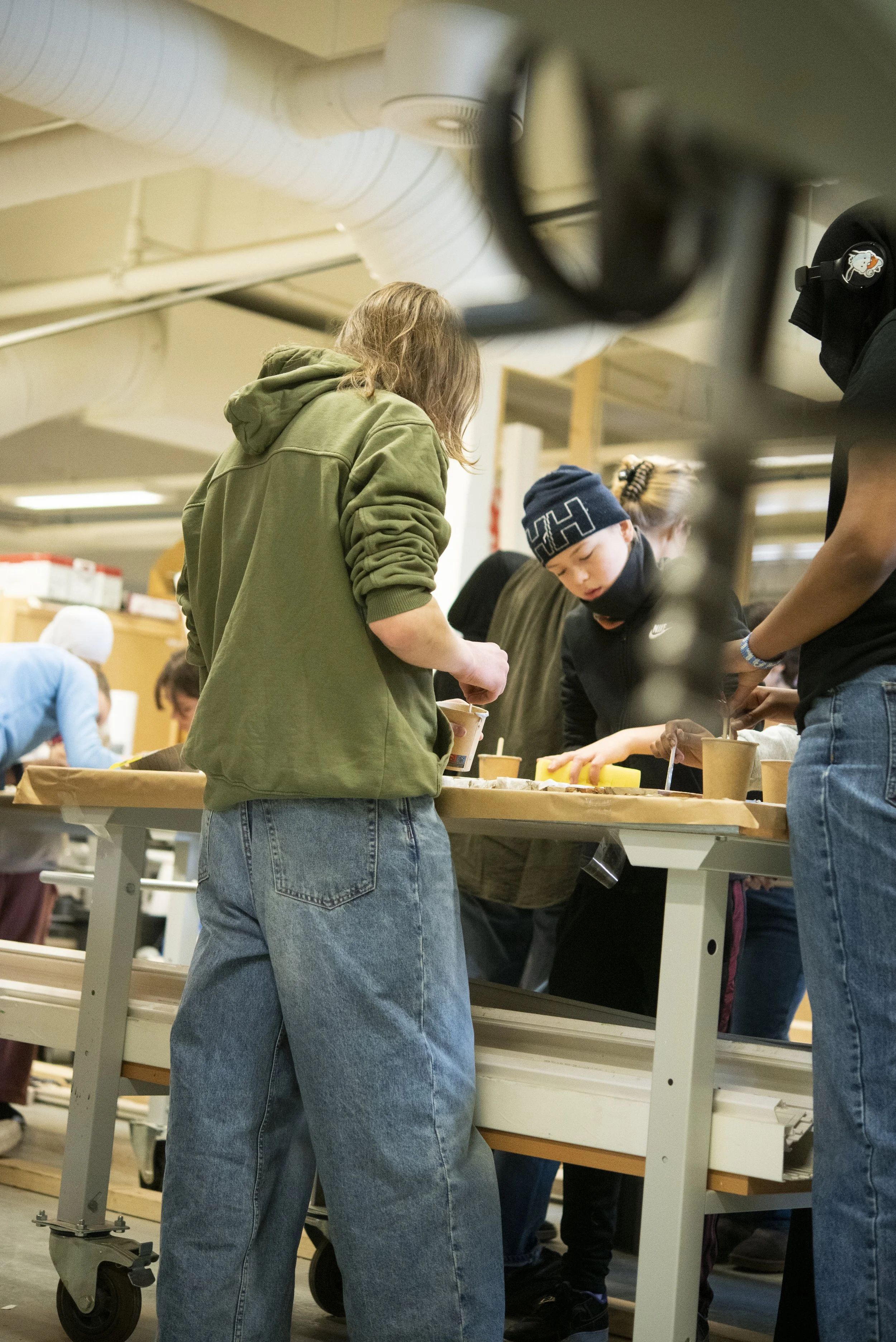 People in casual clothing working at a table in a workshop or classroom.