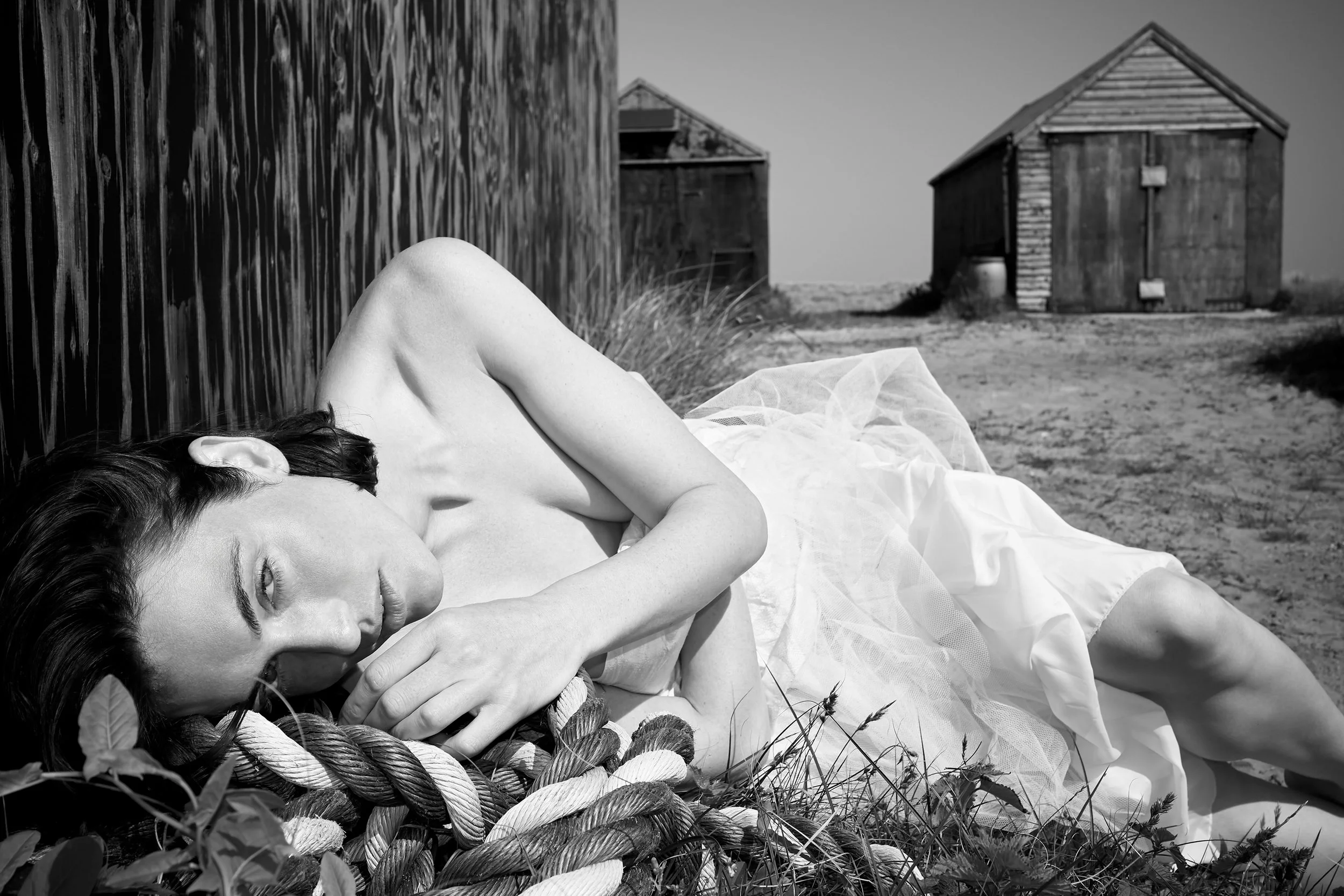 model laying on ropes near a black hut.jpg
