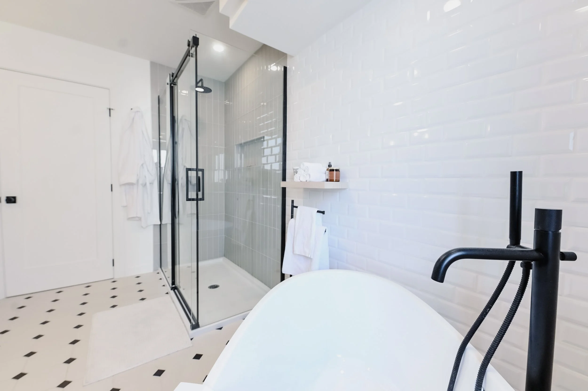 Freestanding bathtub with black faucet against a white brick wall, New York style ensuite in Montreal West