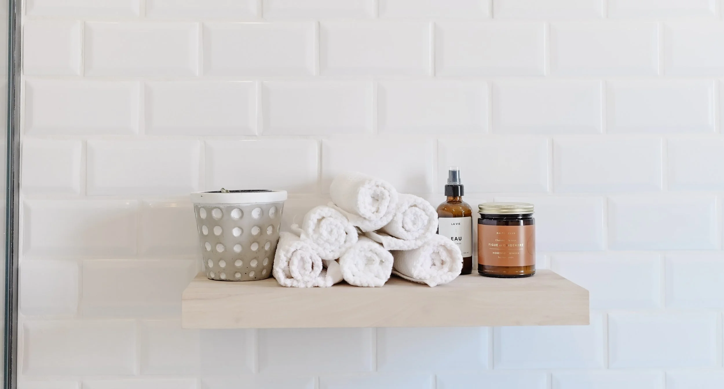 Floating shelf with rolled white towels, potted plant and bath products, New York style ensuite